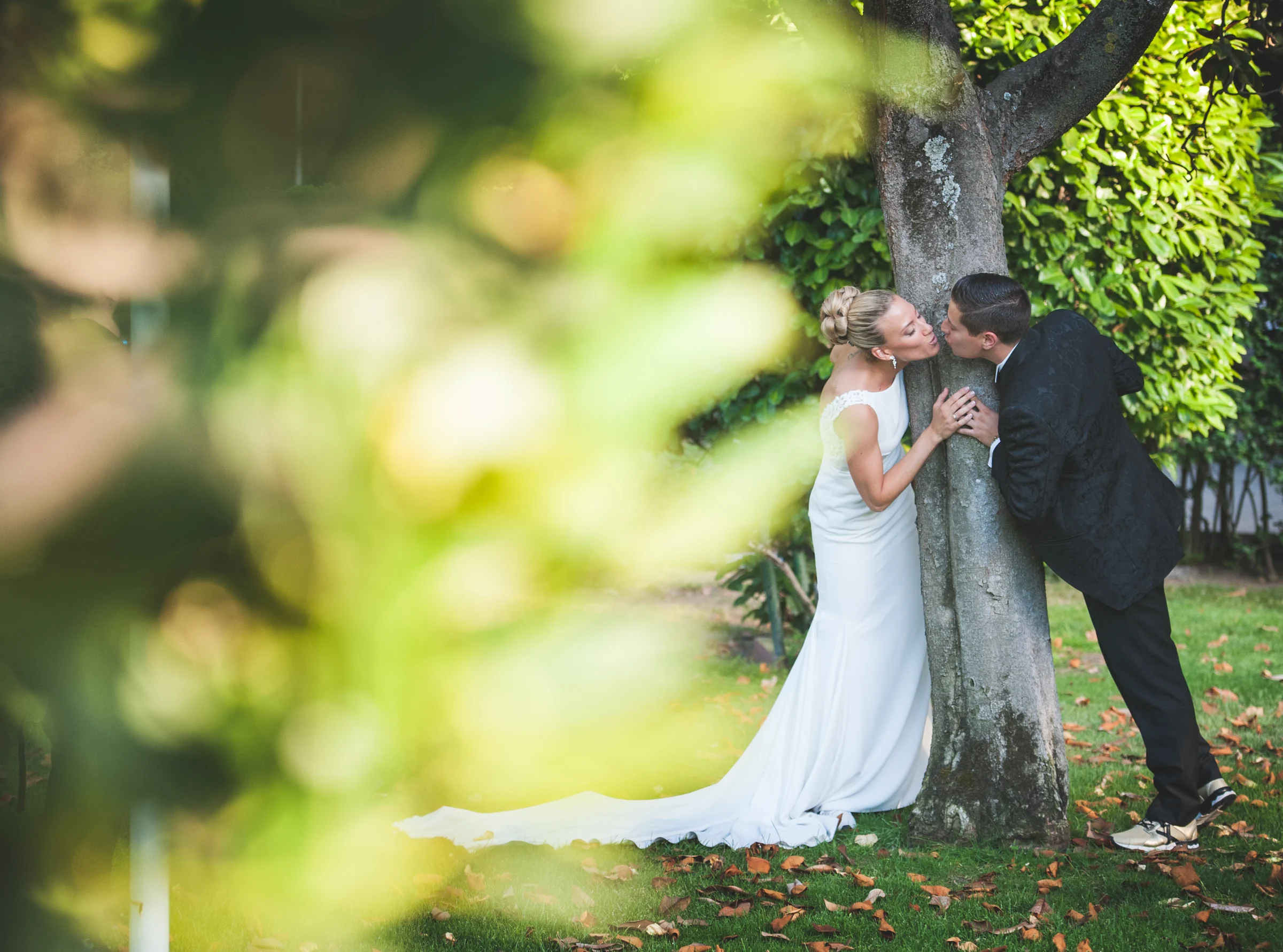 Beso de novios tras hojas desenfocadas durante una boda en Mirador de Cuatro Vientos.