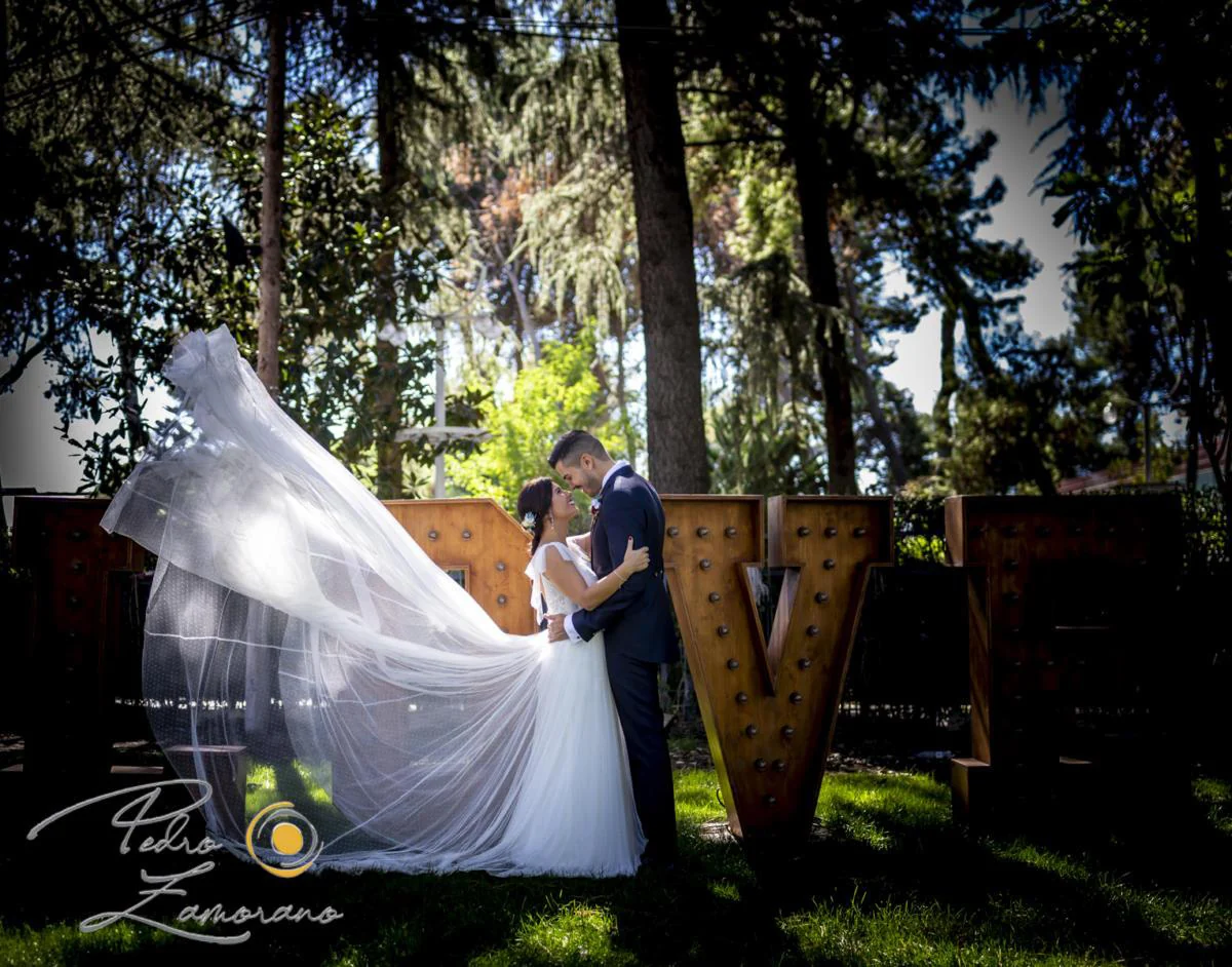 Novios con velo al viento junto a letras decorativas durante una boda en Mirador de Cuatro Vientos.