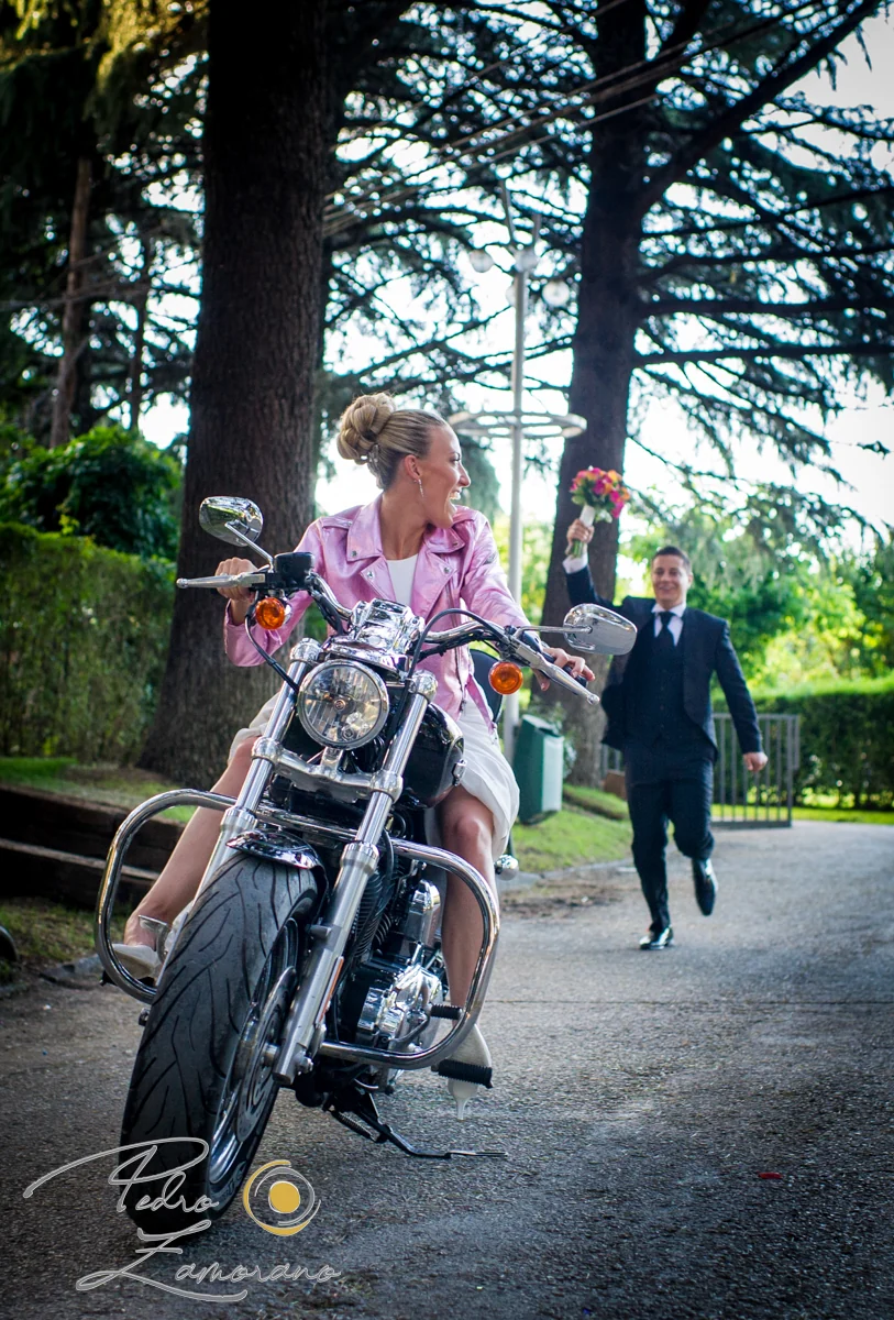 Novia sobre motocicleta y novio al fondo durante una boda en Mirador de Cuatro Vientos.