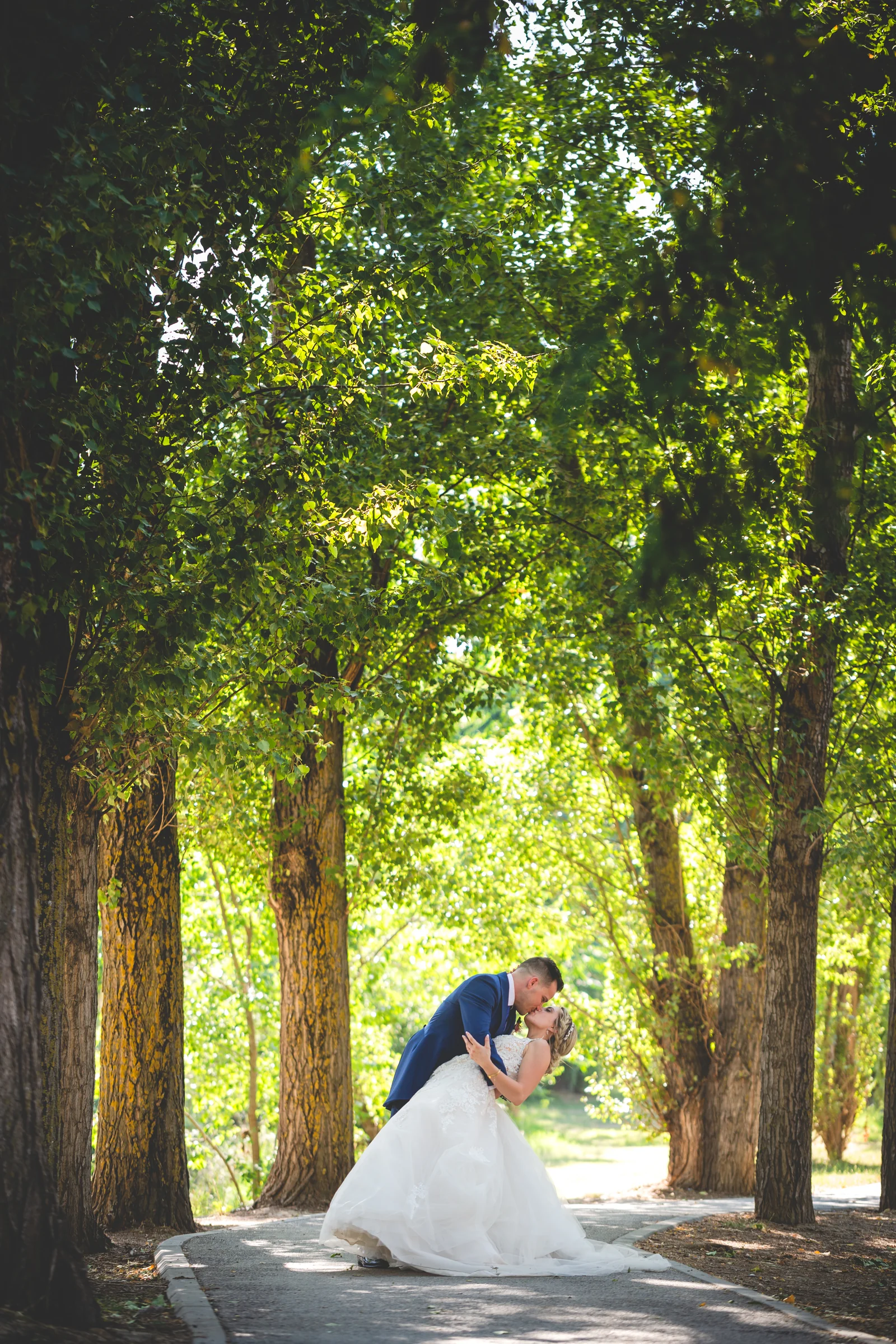 Beso de novios en camino arbolado vertical durante una boda en Mirador de Cuatro Vientos.