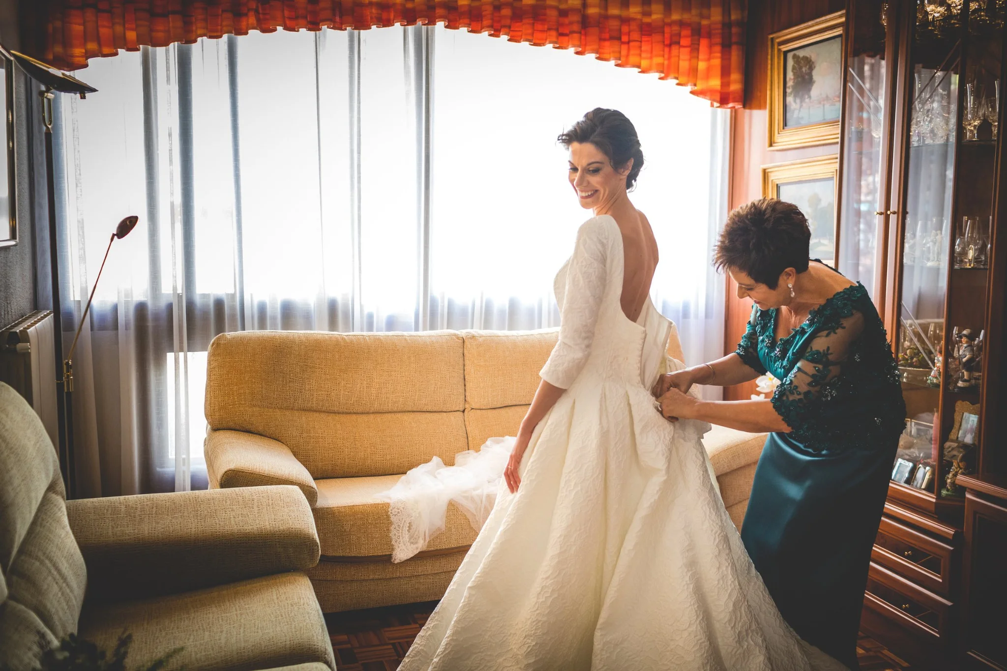 Madre ayudando a vestir a la novia junto a la ventana en una boda en Peñarrubia de Araceli, fotografía de Pedro Zamorano.