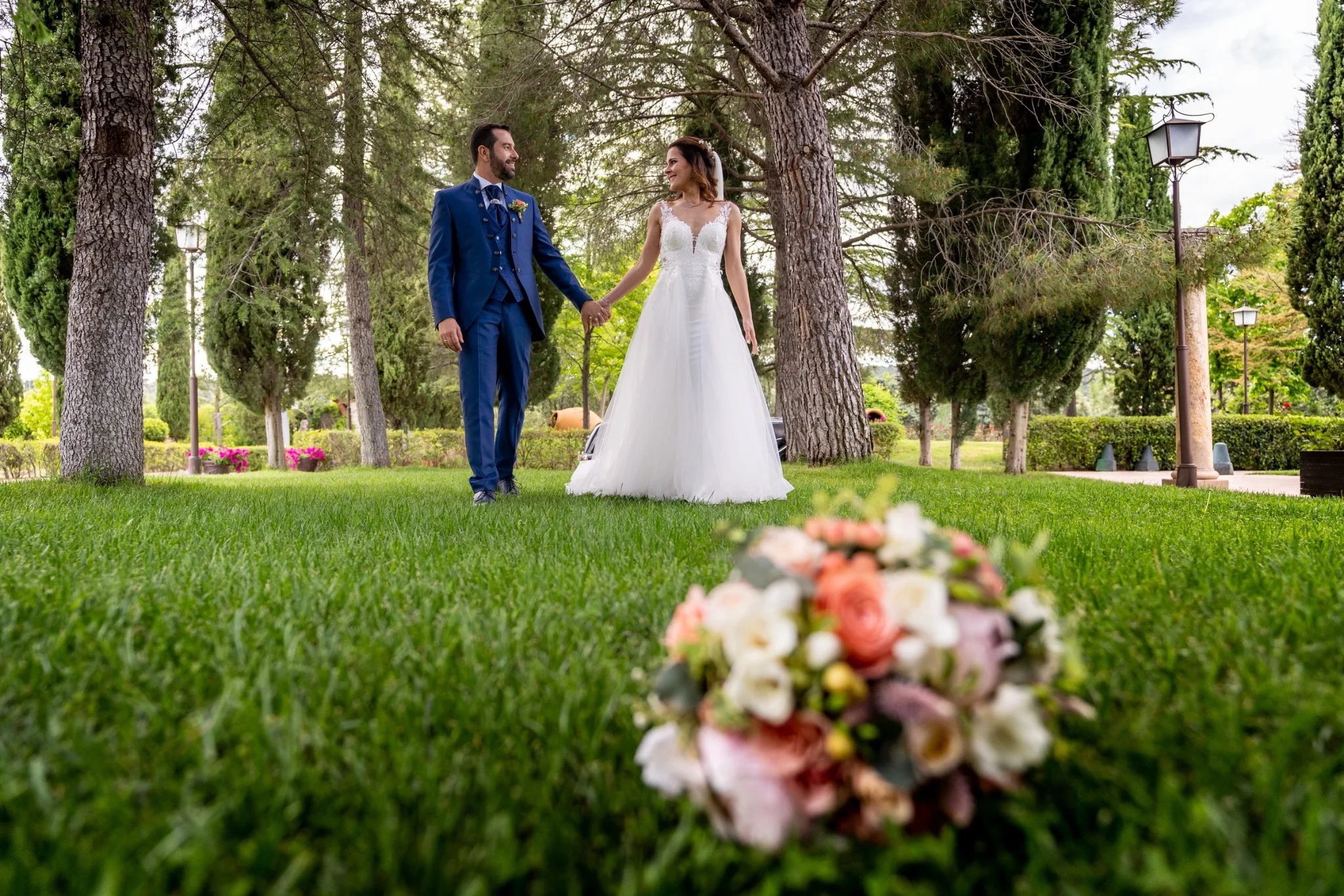 Novios caminando por el jardín con el ramo en primer plano en una boda en Peñarrubia de Araceli, fotografía de Pedro Zamorano.