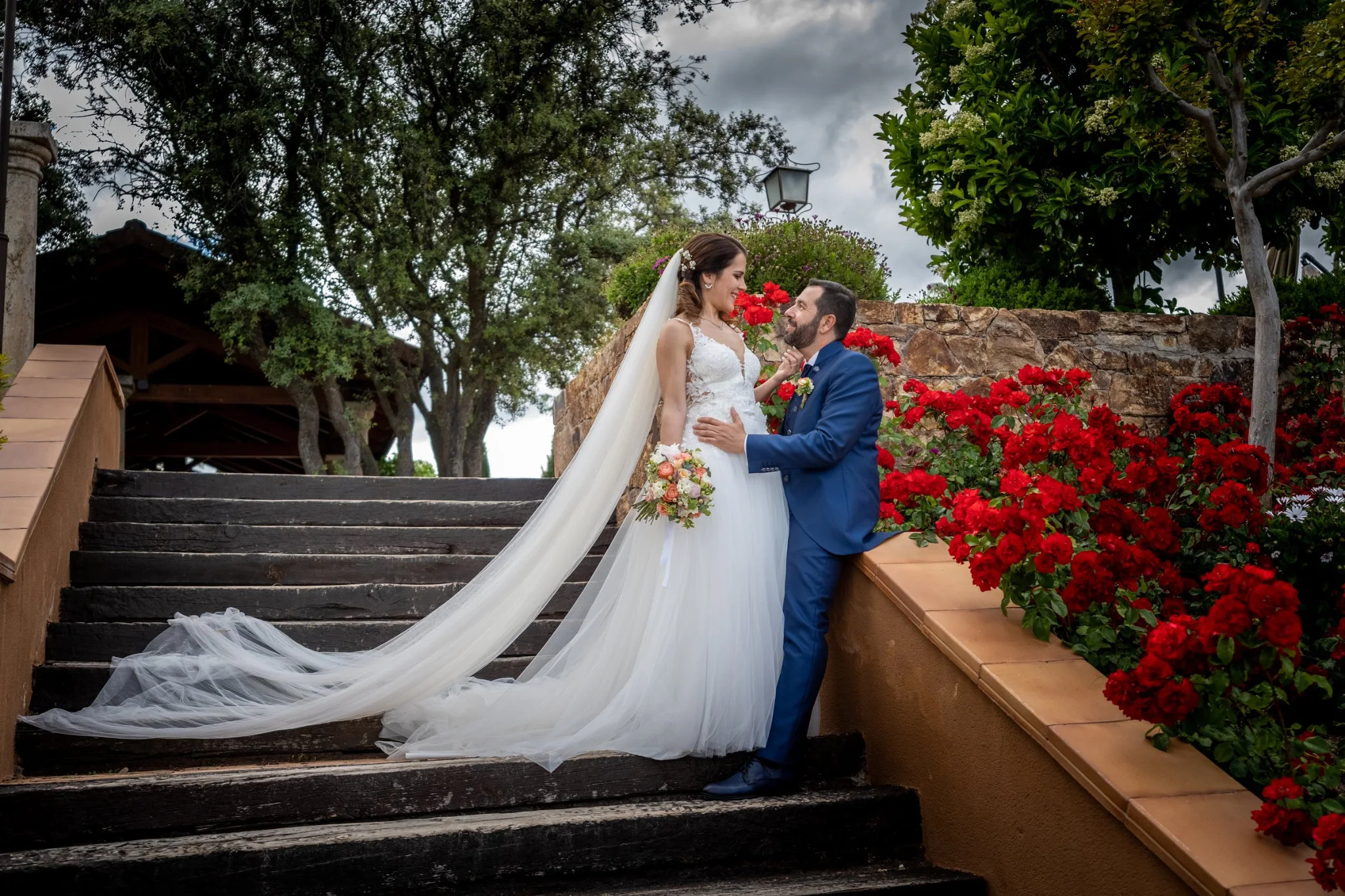 Novios posando en una escalera rodeada de rosas rojas en una boda en Peñarrubia de Araceli, fotografía de Pedro Zamorano.
