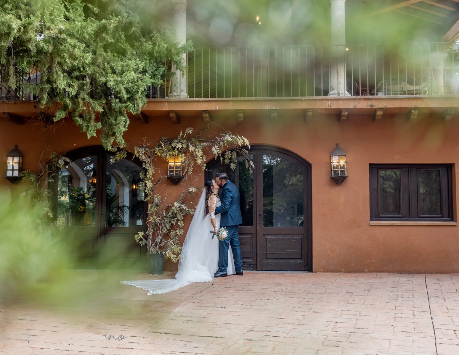 Novios ante la puerta principal vistos entre vegetación en una boda en Peñarrubia de Araceli, fotografía de Pedro Zamorano.
