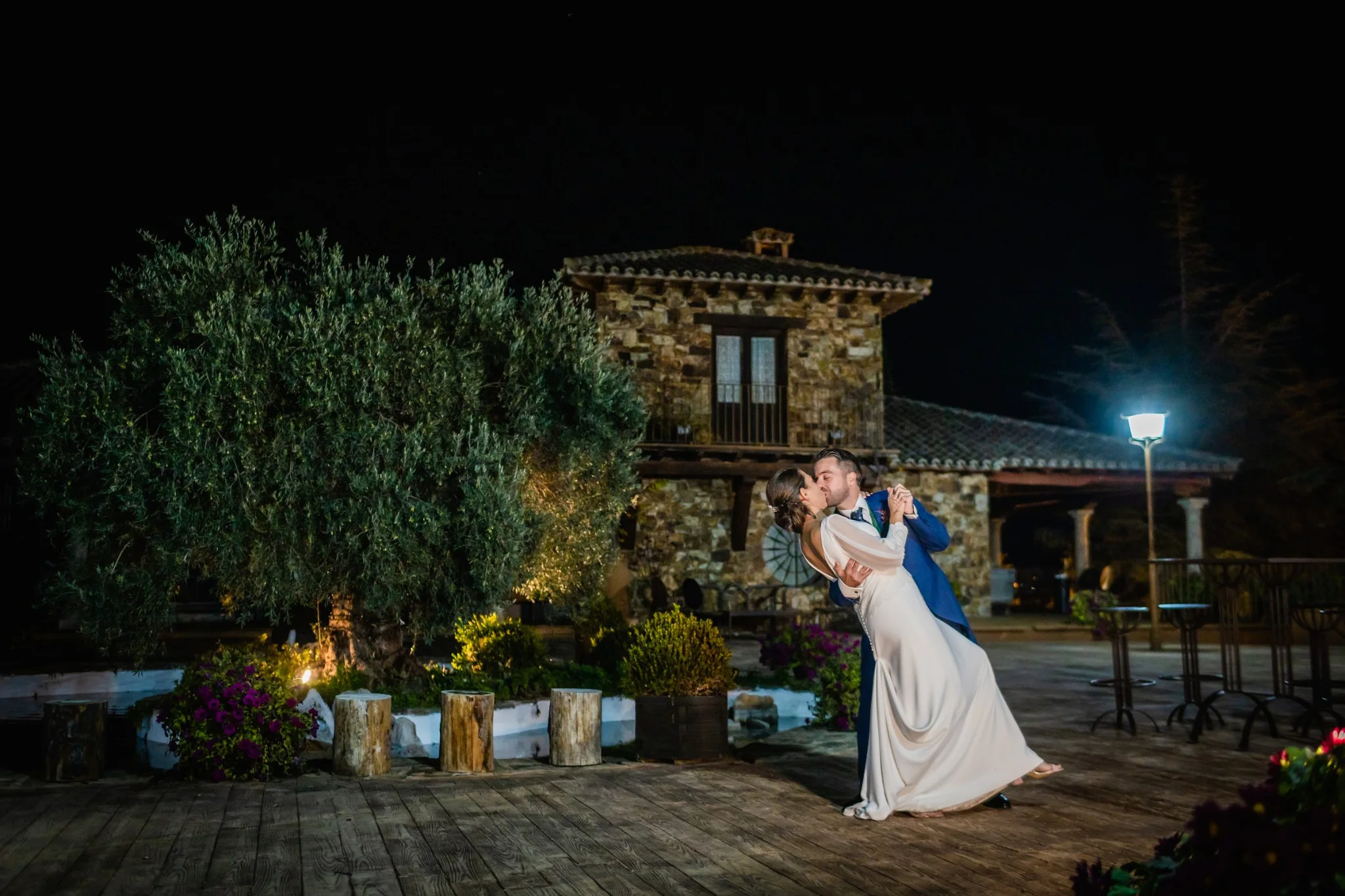 Beso de los novios con la finca iluminada al fondo en una boda en Peñarrubia de Araceli, fotografía de Pedro Zamorano.