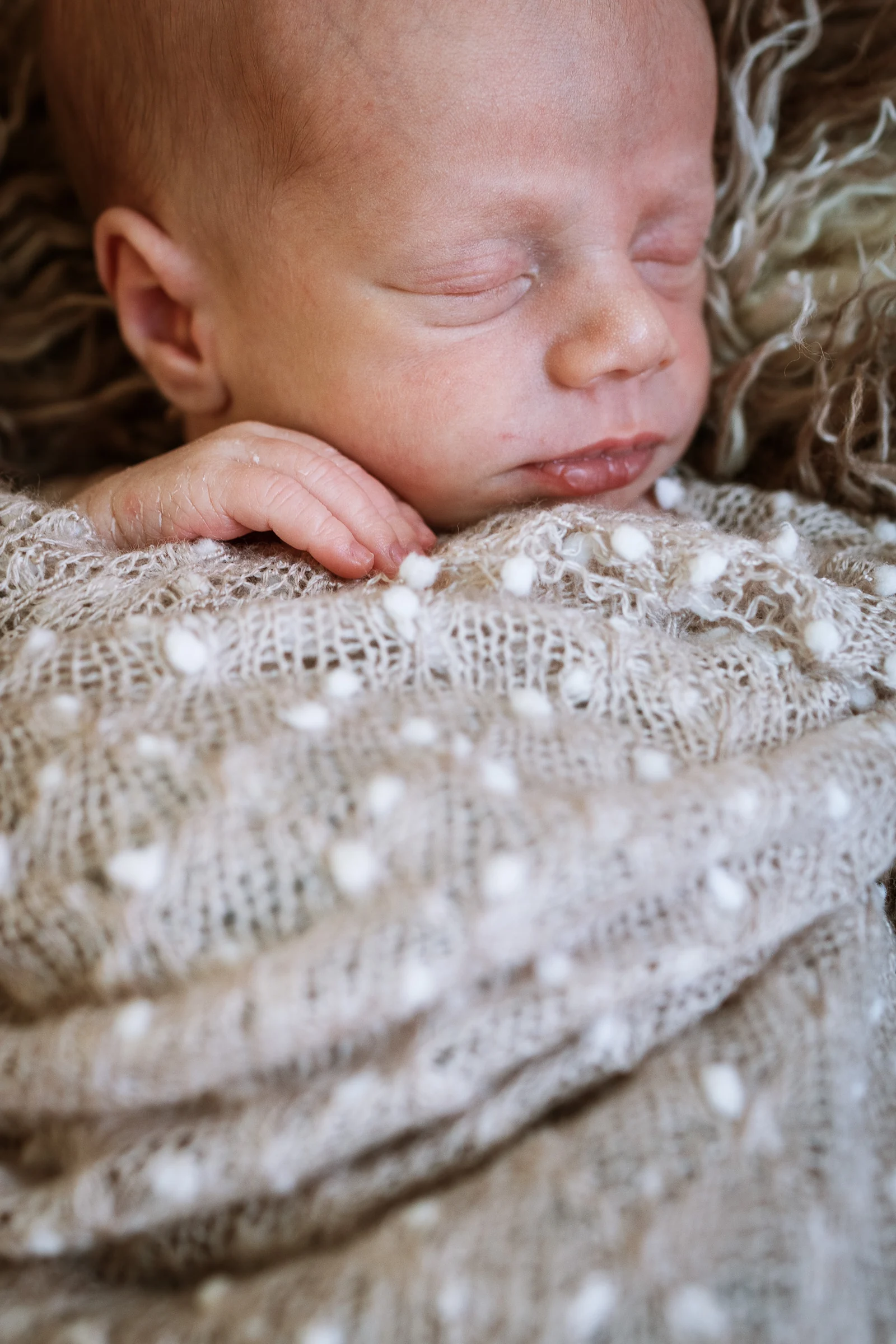Primer plano de recién nacido dormido envuelto en una manta beige durante una sesión newborn en estudio.