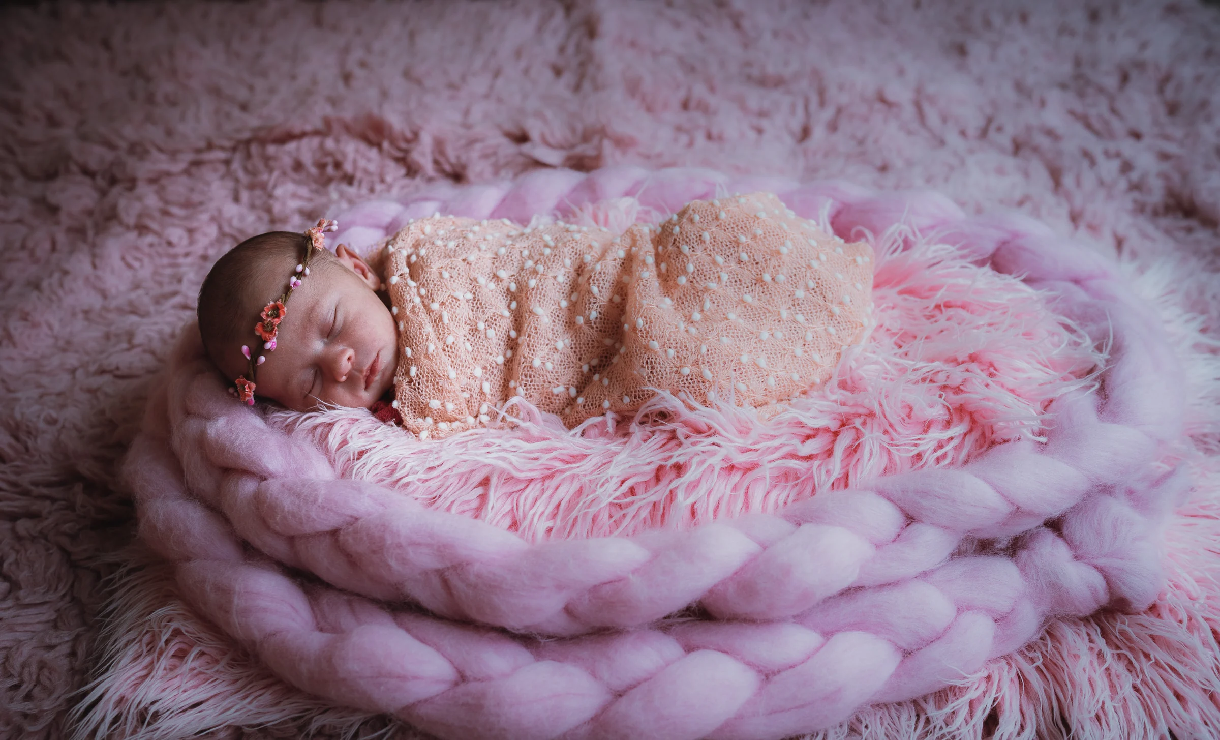 Recién nacido dormido sobre una manta rosa de punto grueso en una sesión newborn.