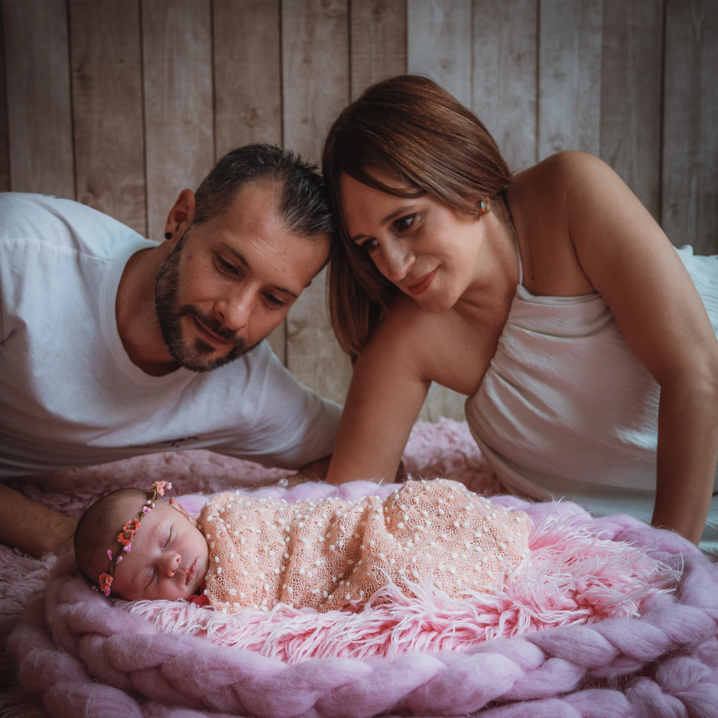 Padre y madre junto a su recién nacida dormida sobre una manta rosa en estudio.