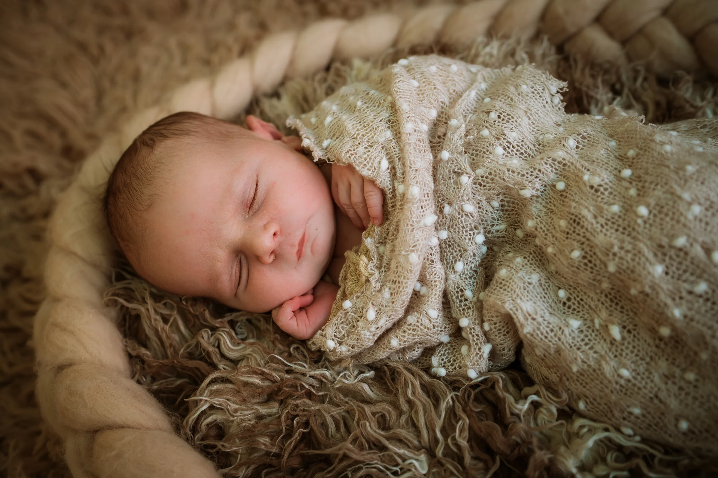 Recién nacido dormido en una cesta con manta beige durante una sesión newborn.