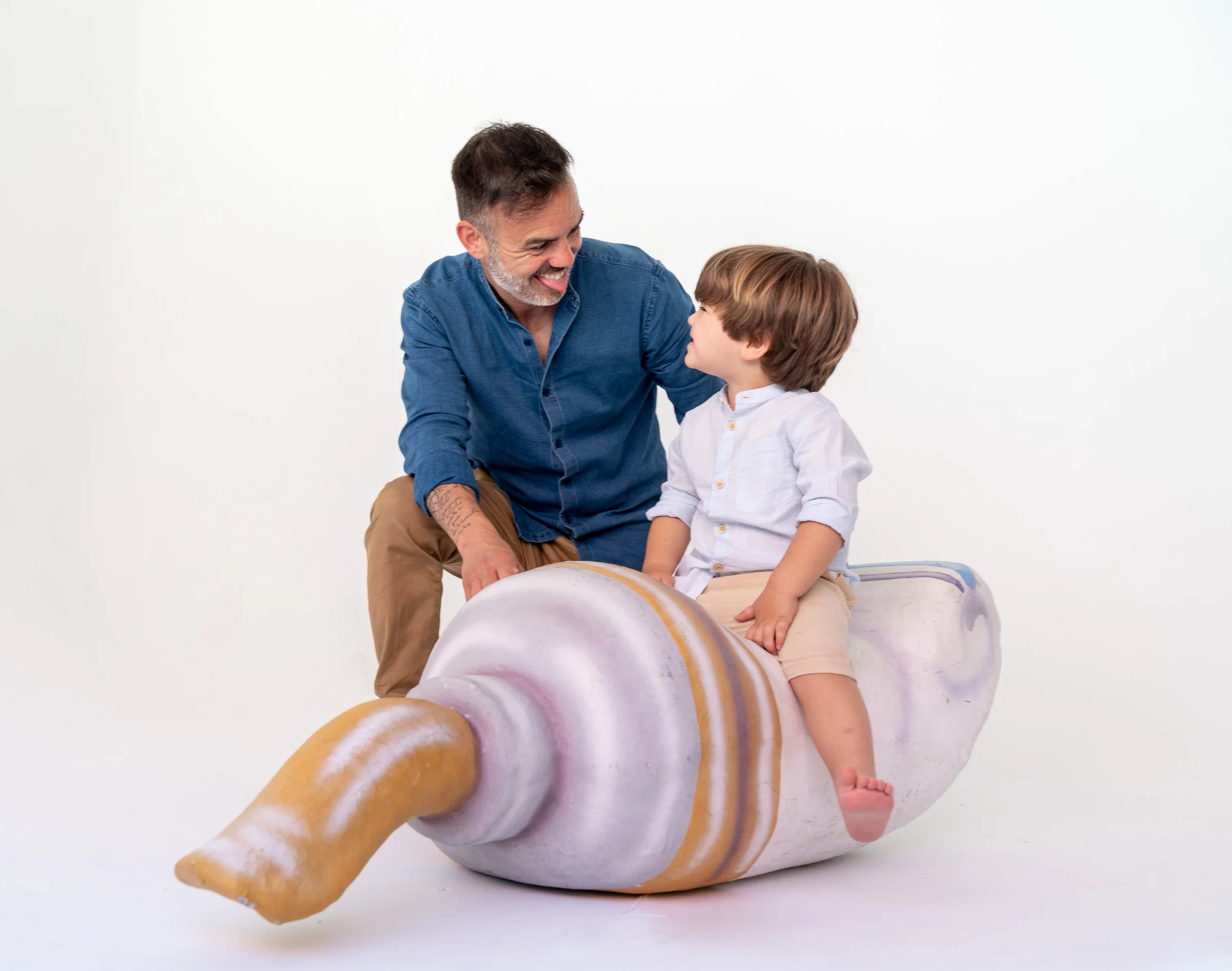 Padre e hijo posan en estudio sobre un atrezo con forma de caracola en fondo blanco.