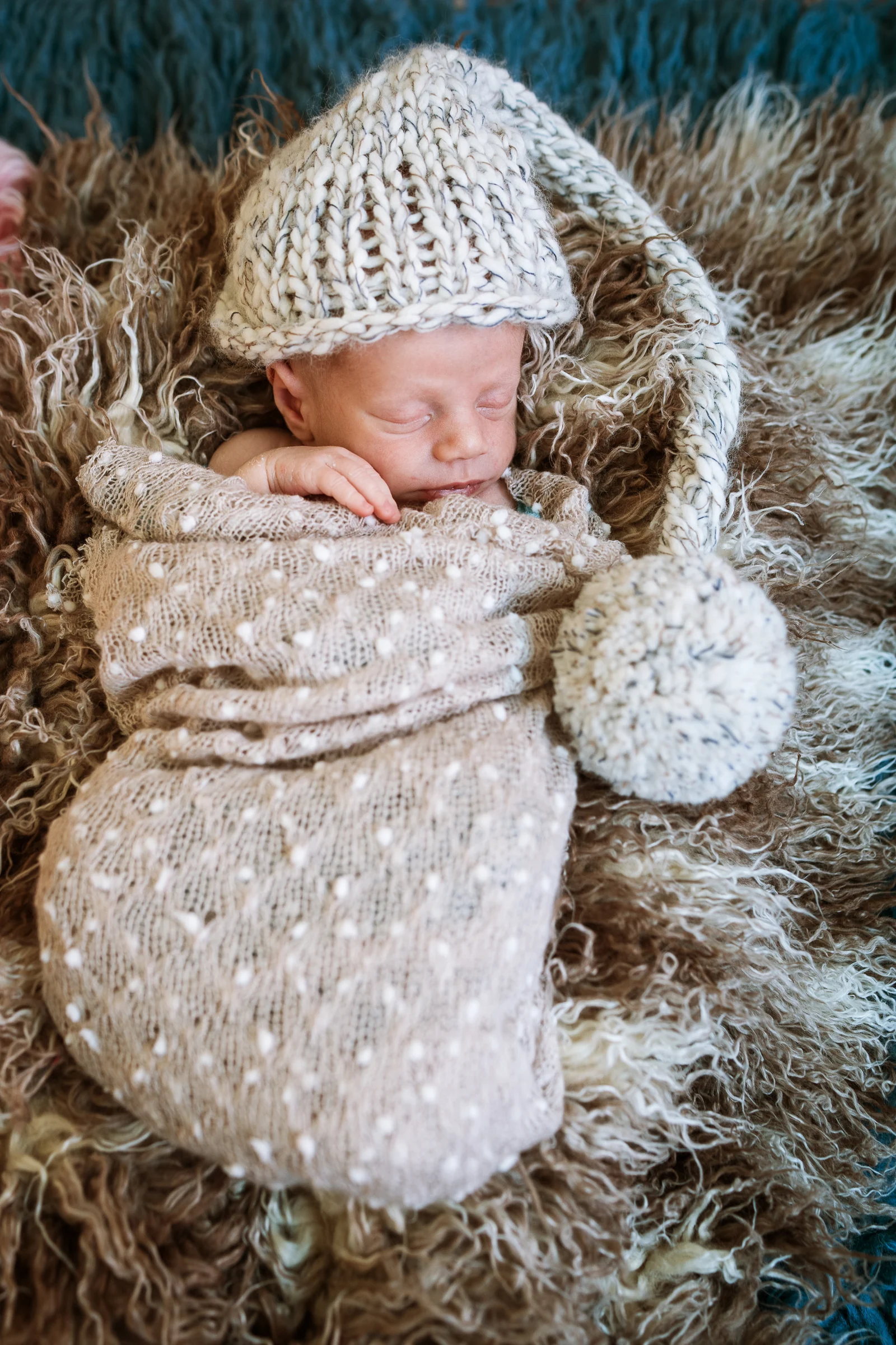 Recién nacido dormido dentro de un saco de punto con gorrito y pompón.