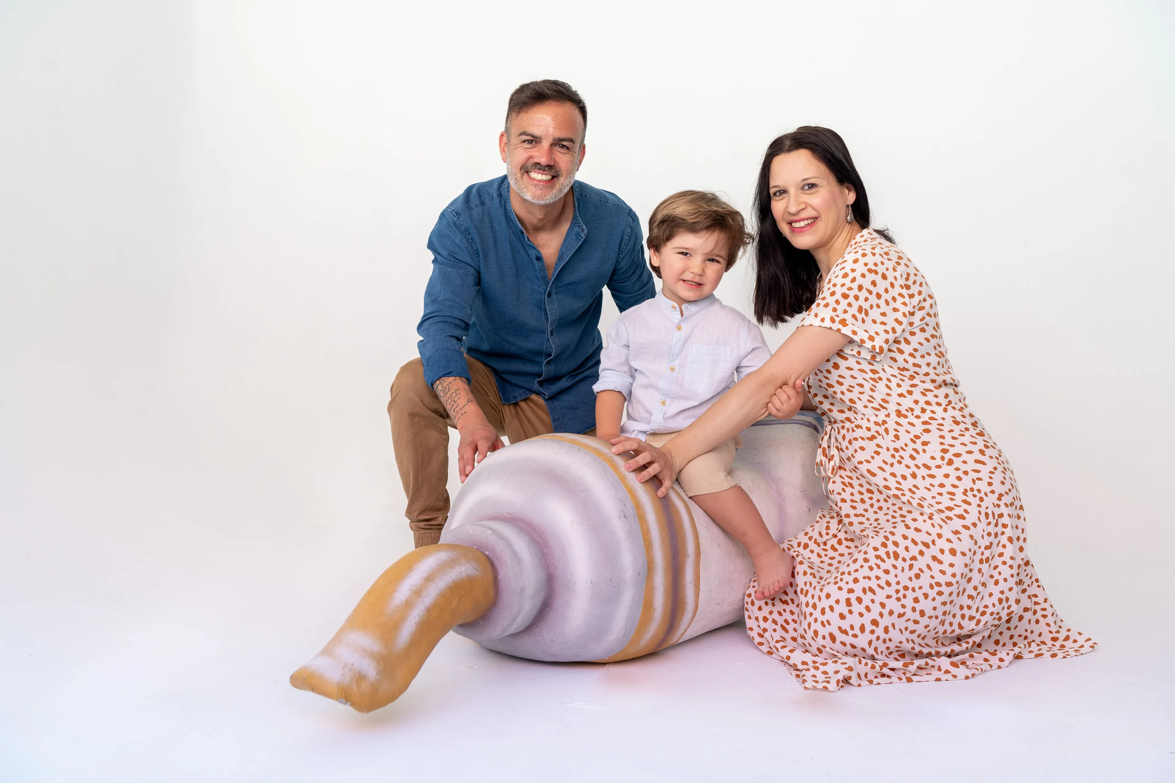 Familia con un niño pequeño posando junto a un recién nacido en estudio blanco.