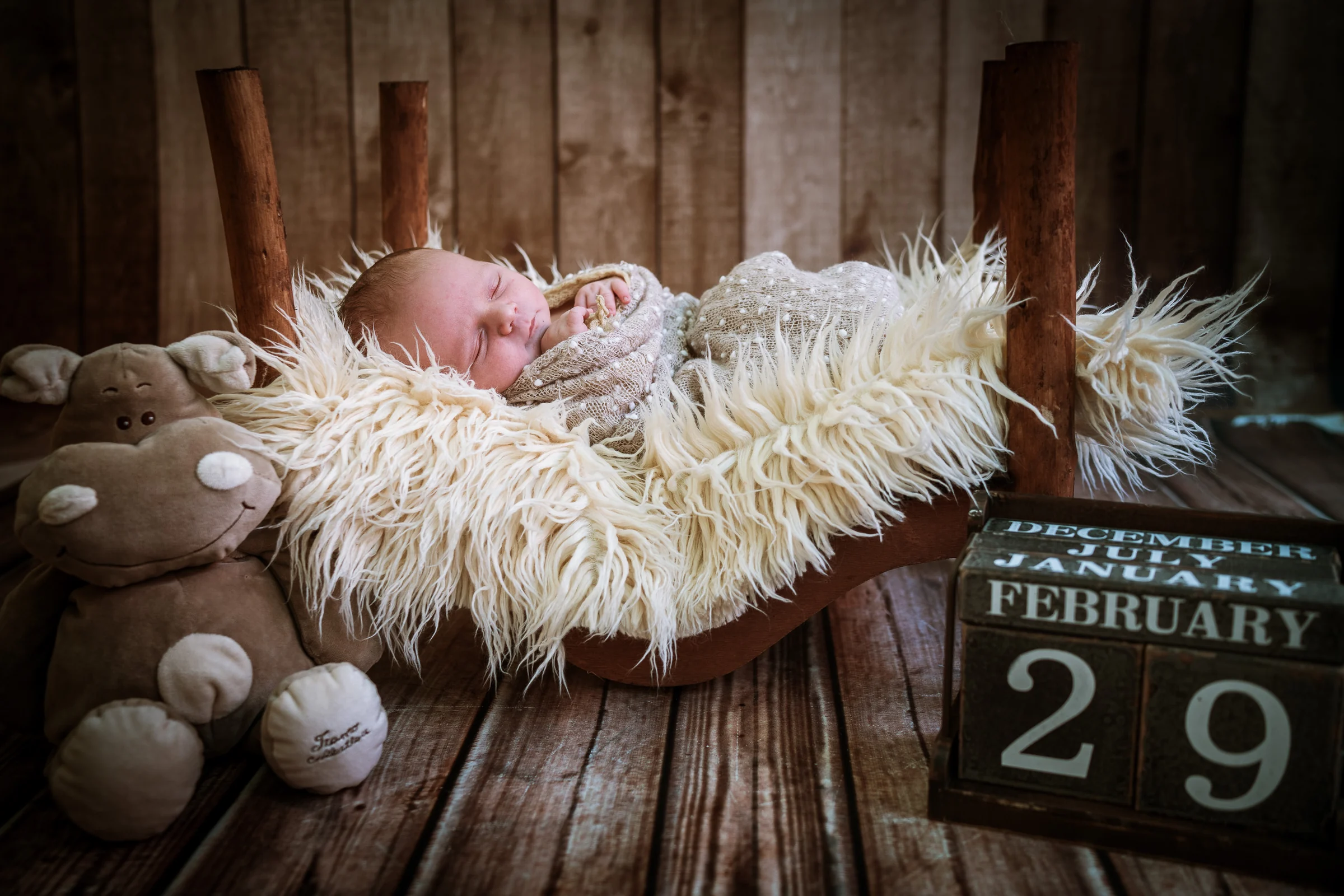 Recién nacido dormido en una pequeña cama peluda con calendario decorativo.