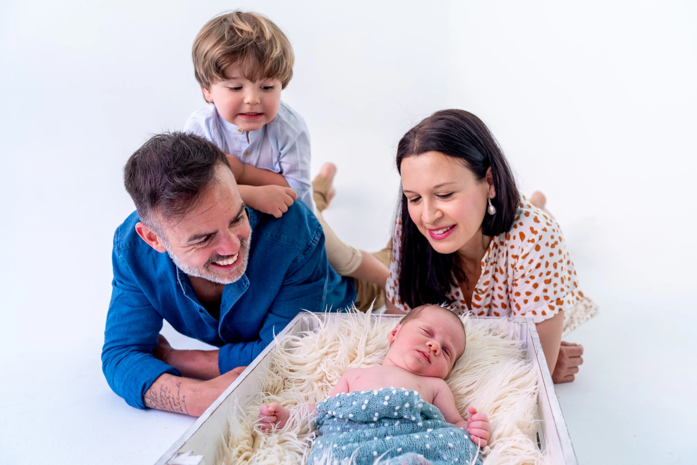 Familia reunida alrededor de su bebé en una fotografía newborn en estudio.