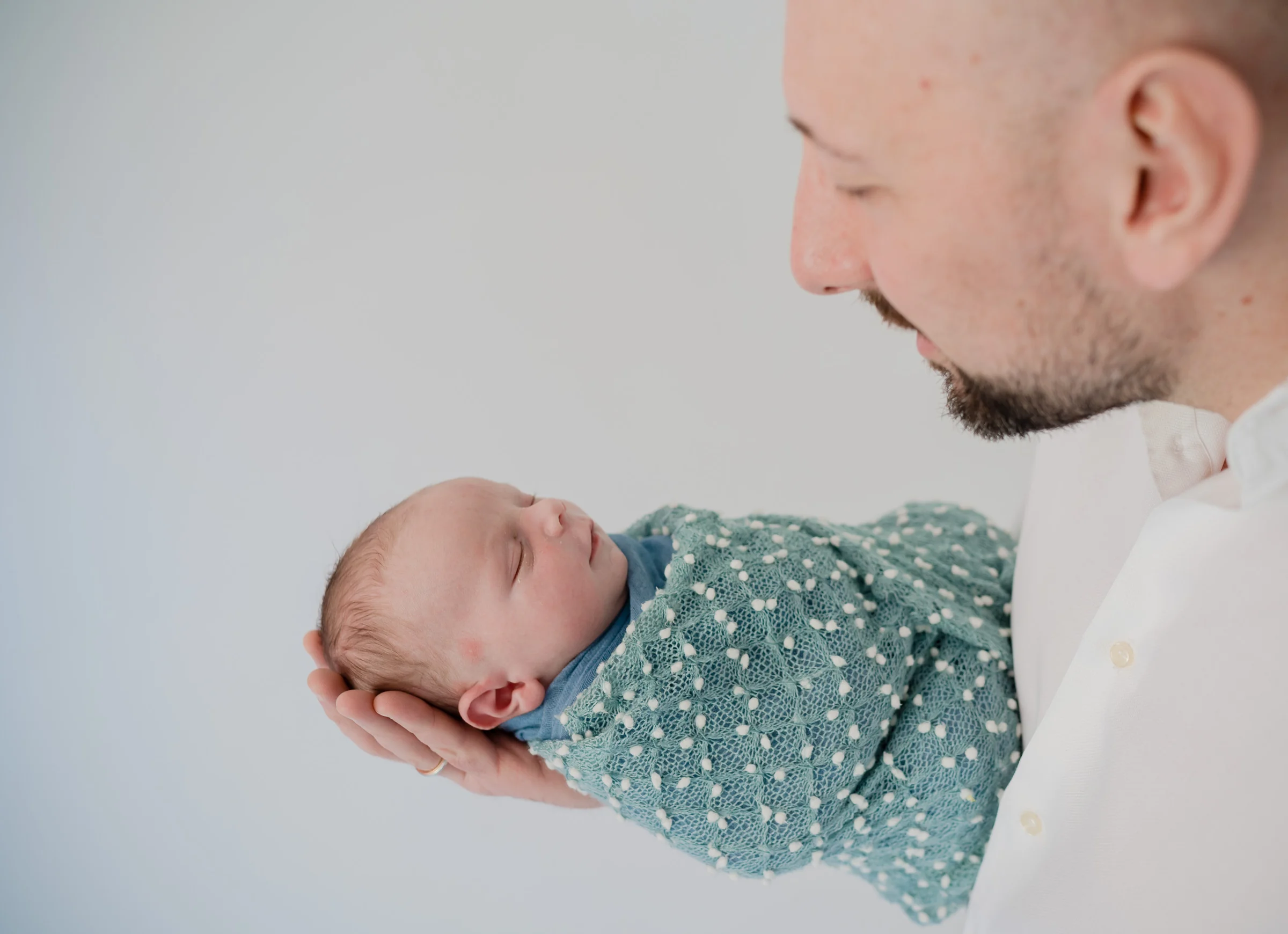 Madre sonríe mientras sostiene al bebé y mira al padre en un retrato familiar.