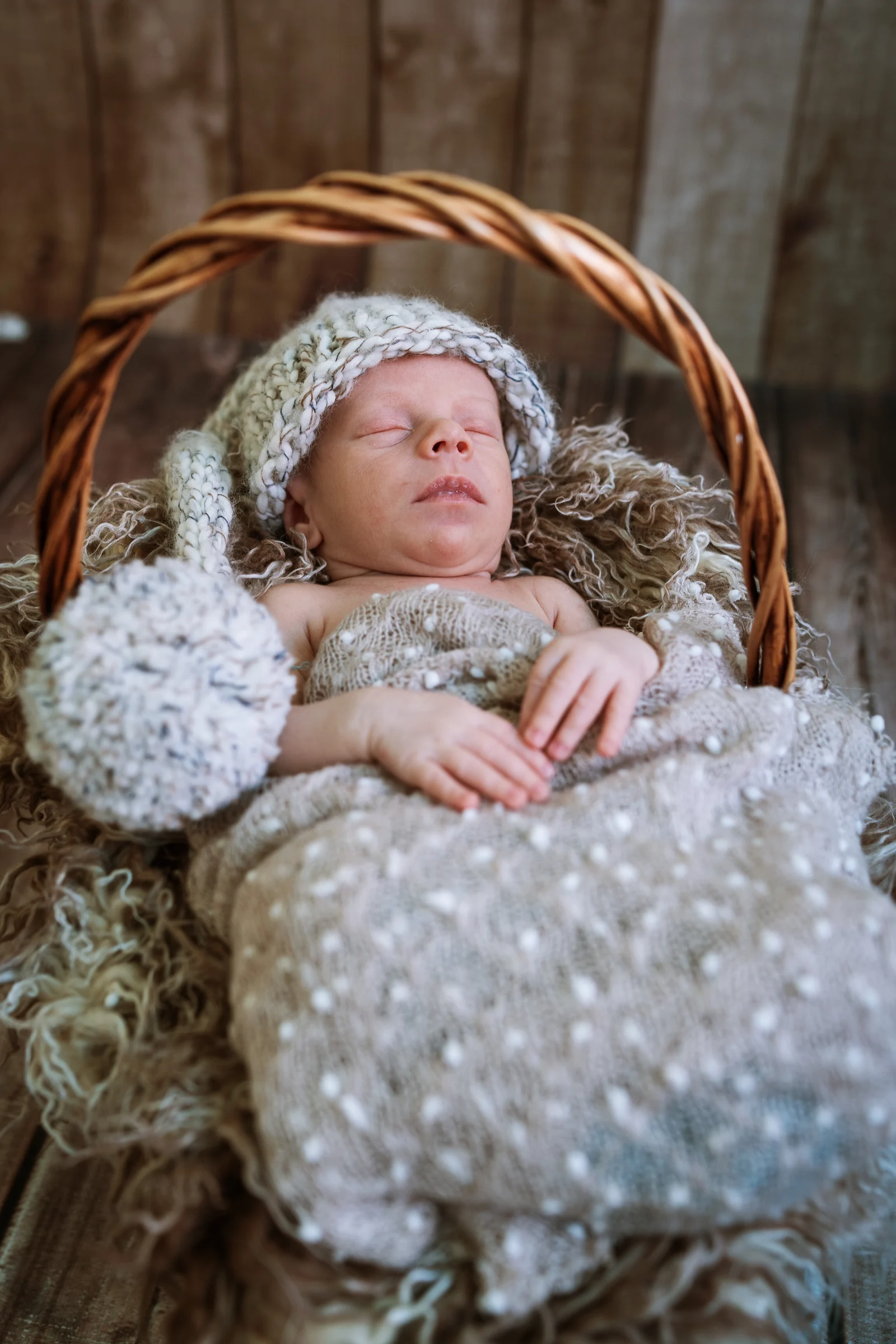 Recién nacido dormido en un capazo de mimbre con gorro de punto y pompón.