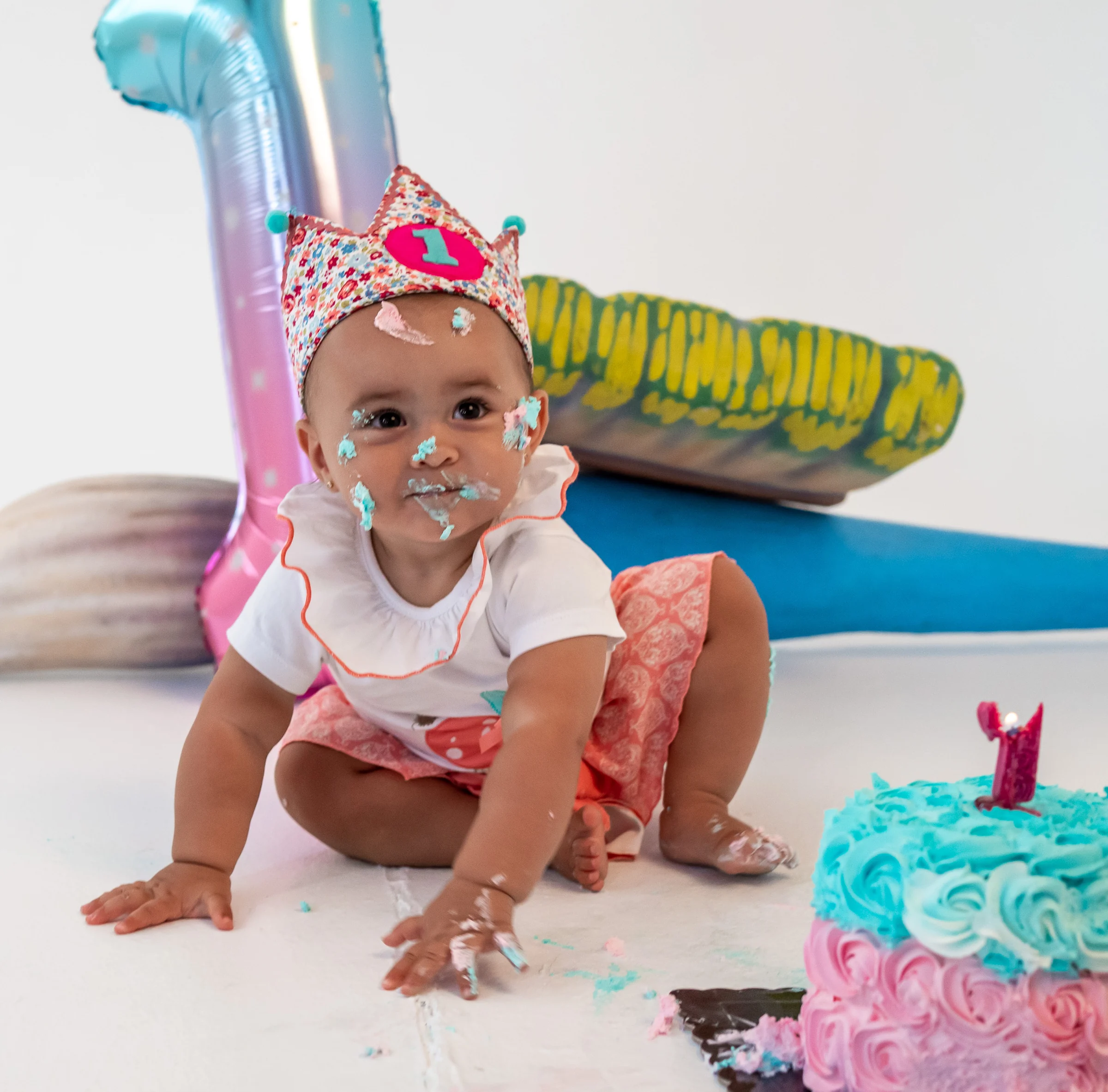 Niña pequeña gateando junto a una tarta de cumpleaños y globos en estudio.