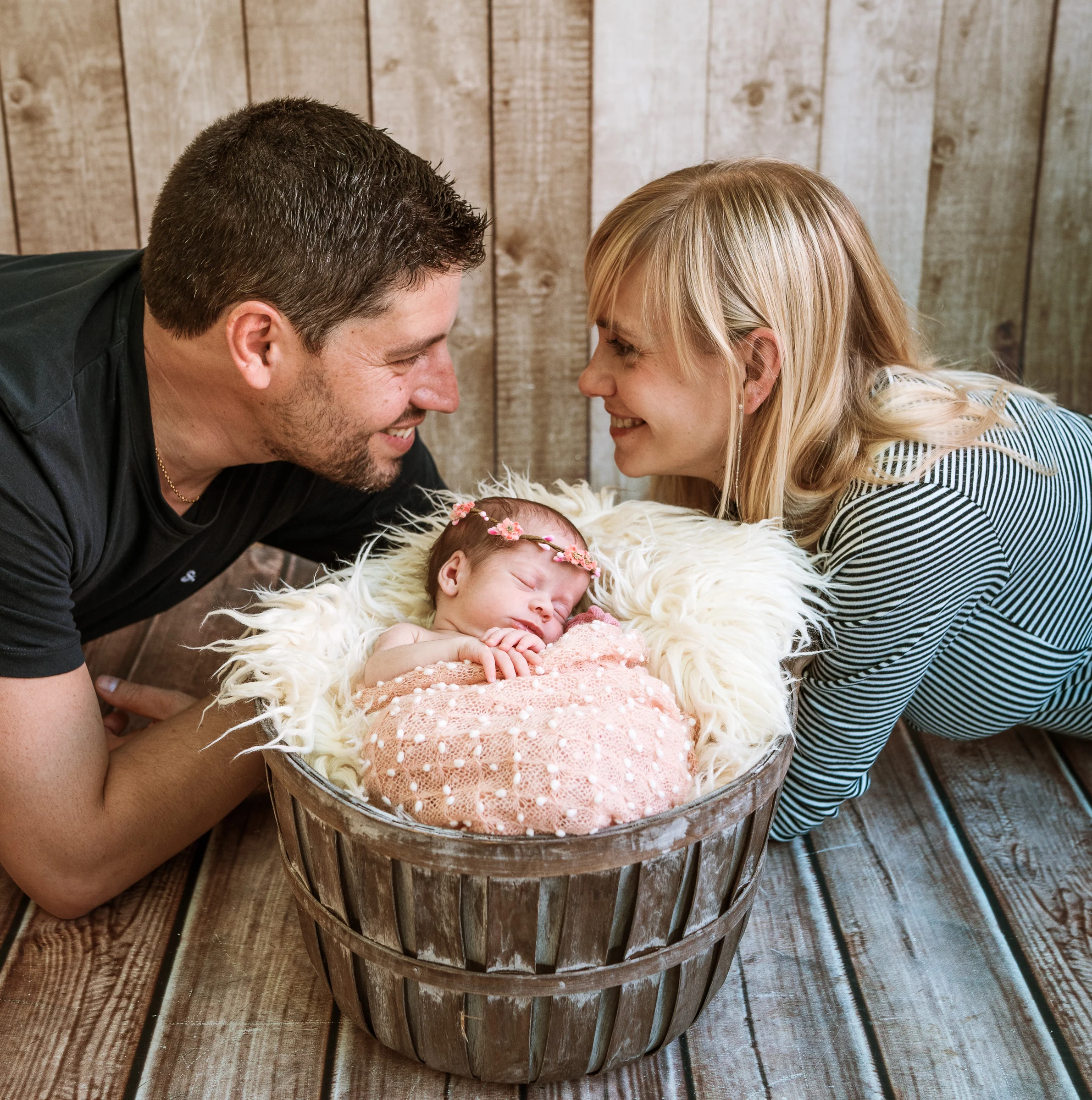 Padres se acercan a su bebé en una cubeta de madera durante la sesión newborn.