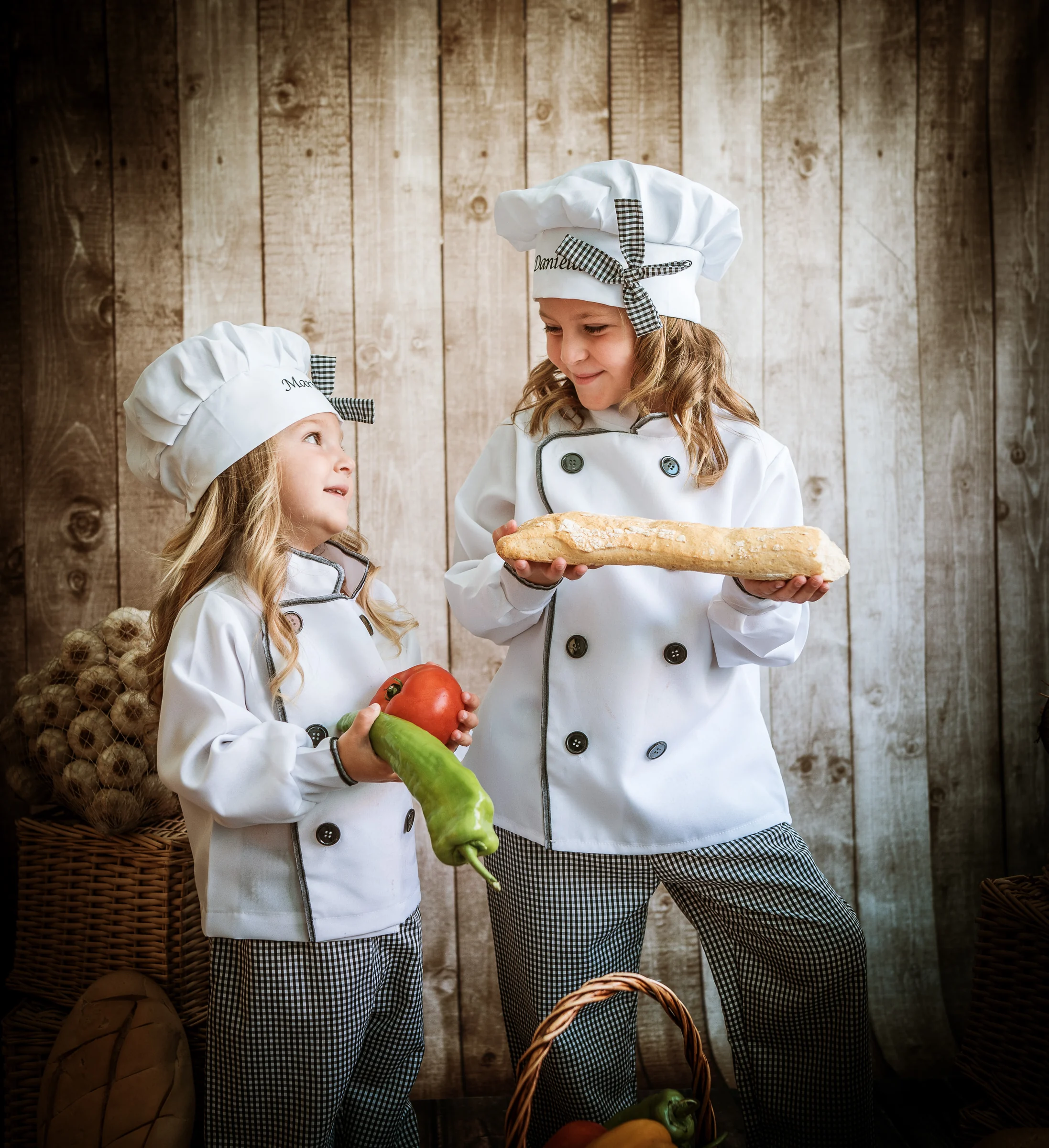 Dos niñas cocineras posan junto a una olla grande y hortalizas.