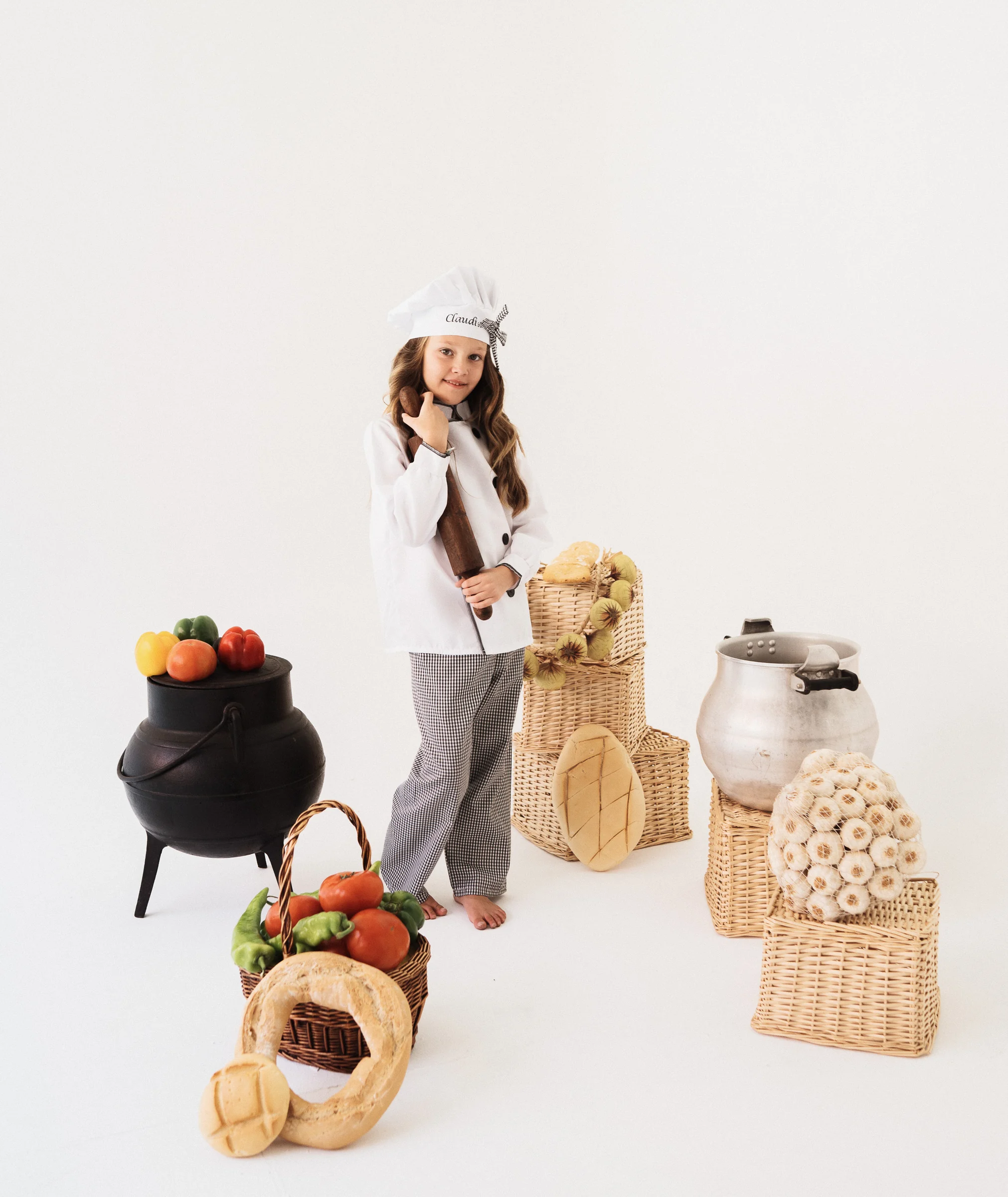 Niña cocinera posando con atrezzo de cocina y verduras sobre fondo blanco.