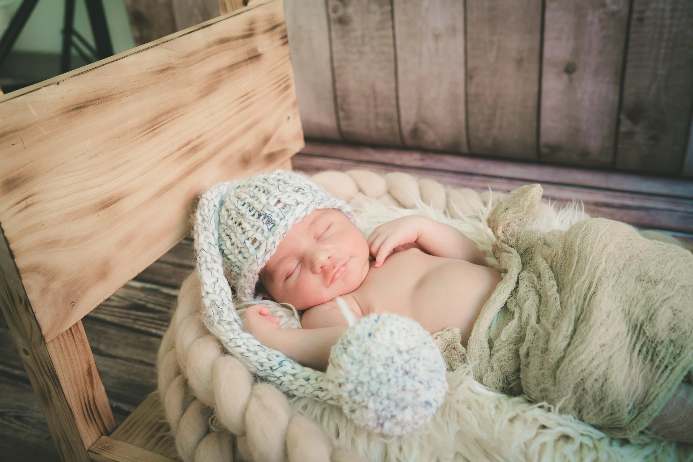 Recién nacido dormido en cesta de mimbre con manta morada y gorrito a juego.