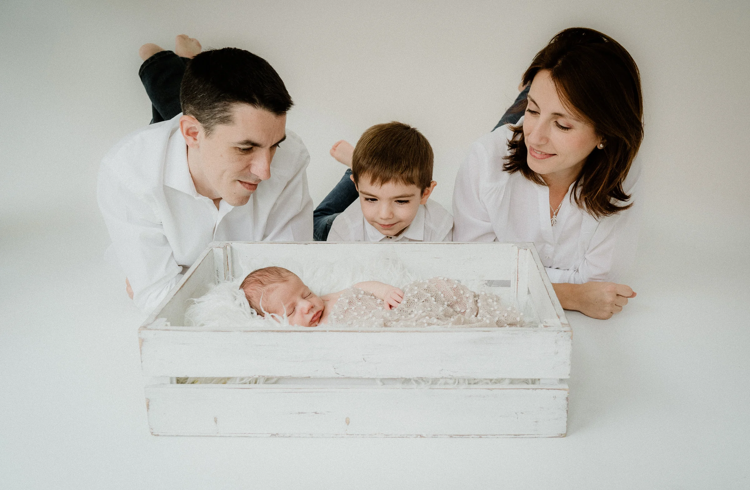 Familia de cuatro posa con el recién nacido sobre un fondo blanco y luminoso.