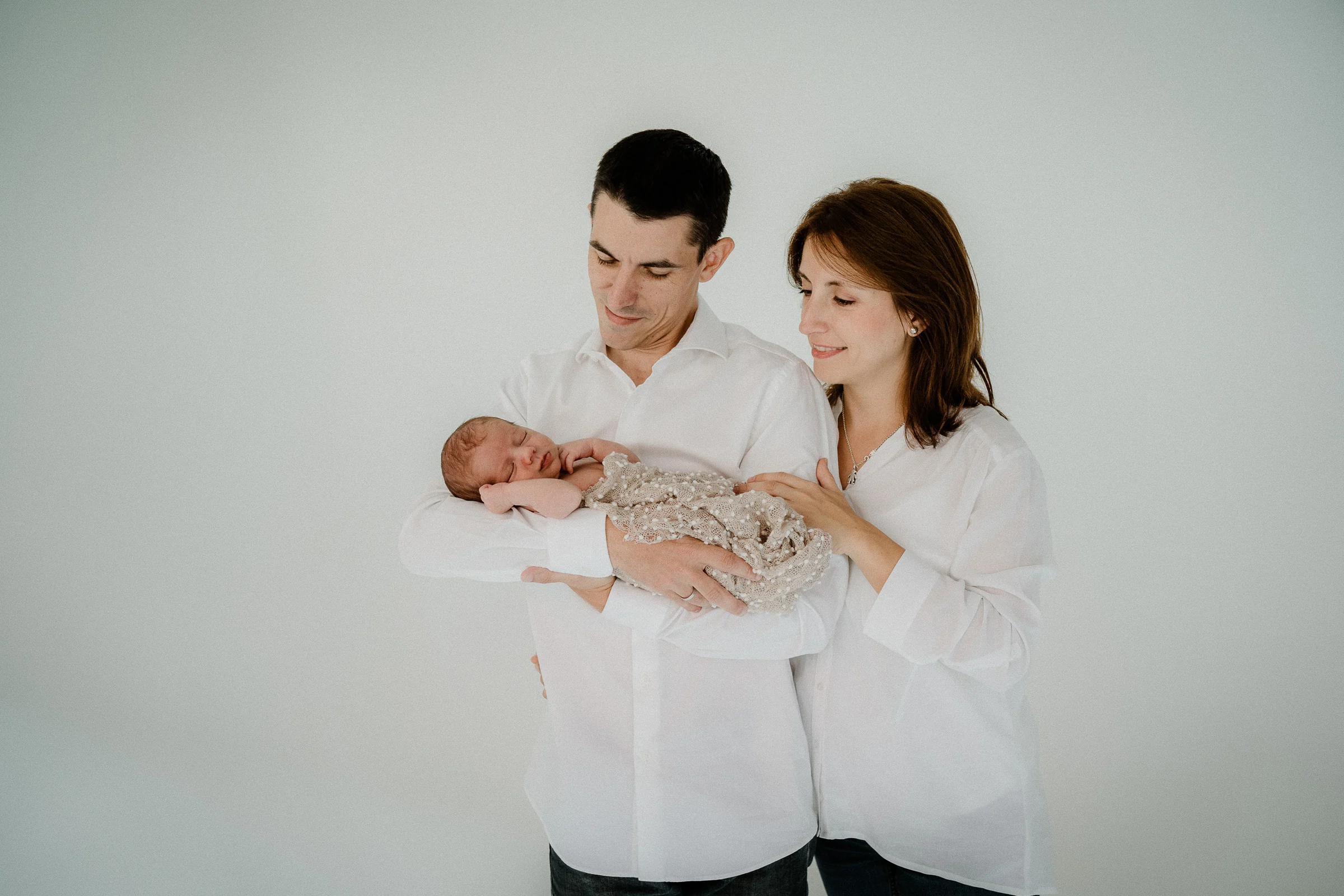 Padre y madre sostienen a su recién nacido en una fotografía minimalista de estudio.