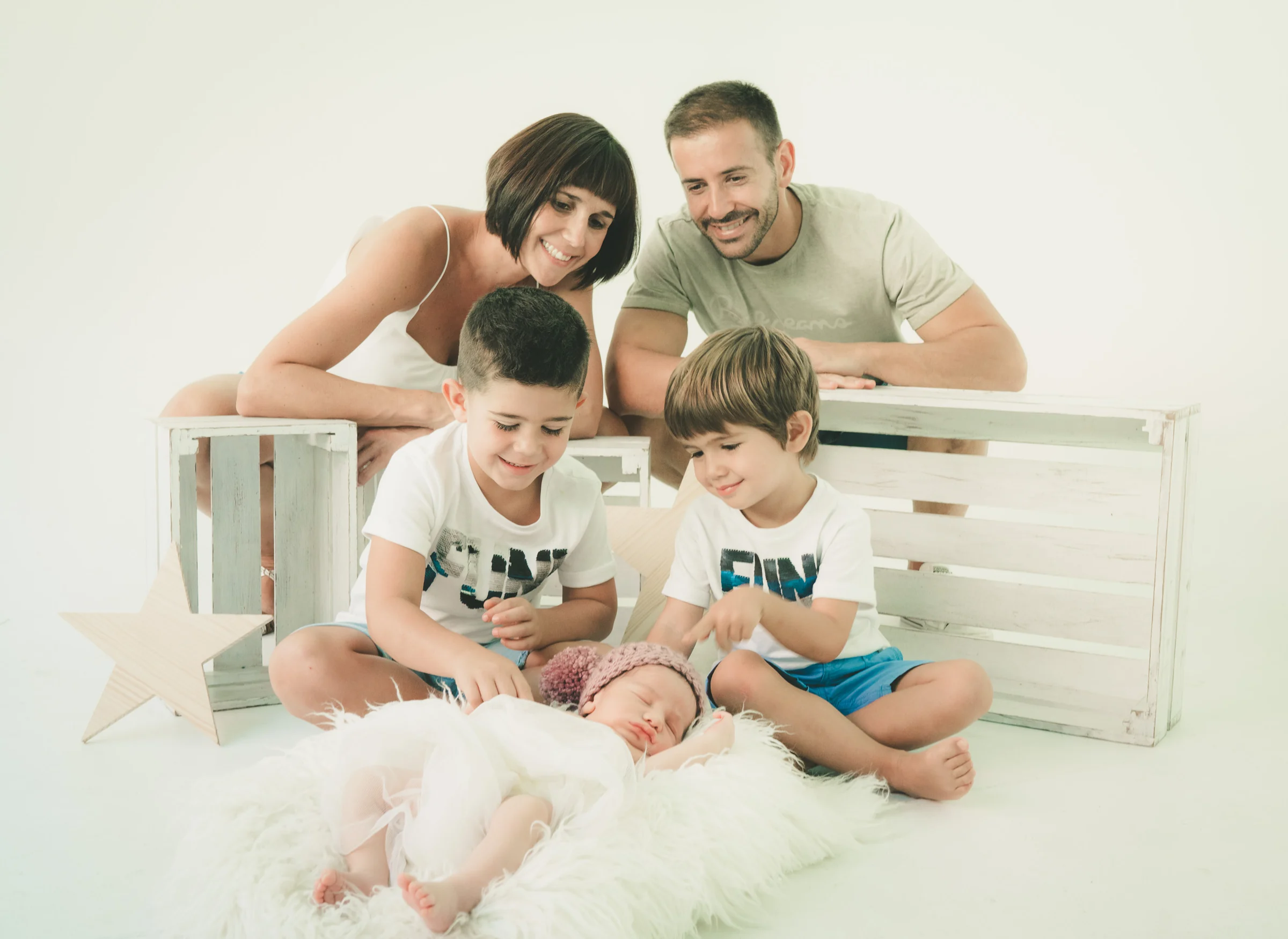Familia de cuatro sentada junto al recién nacido en un retrato sobre fondo blanco.