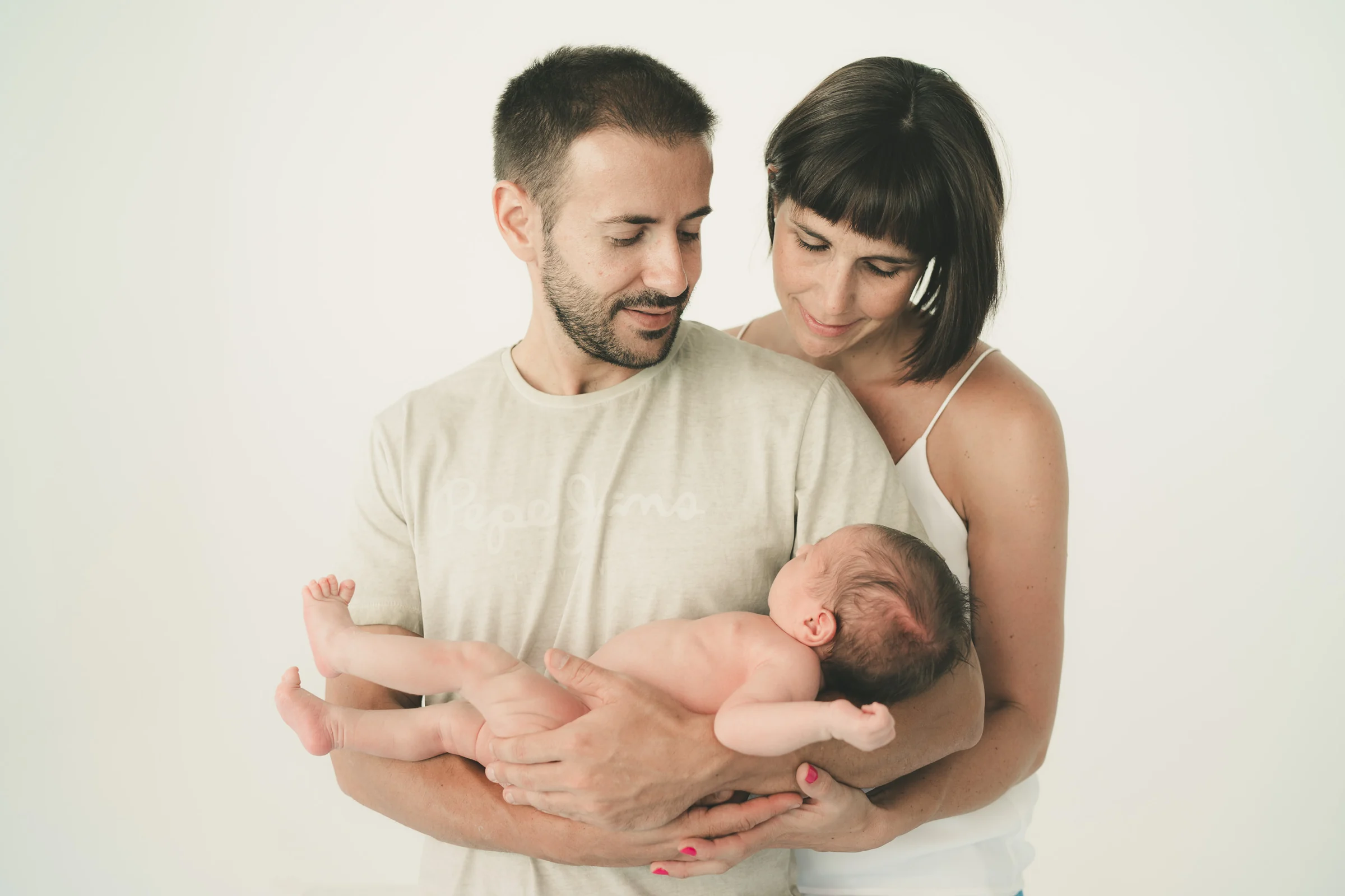 Padre y madre posan con su recién nacido en un retrato familiar de estudio.