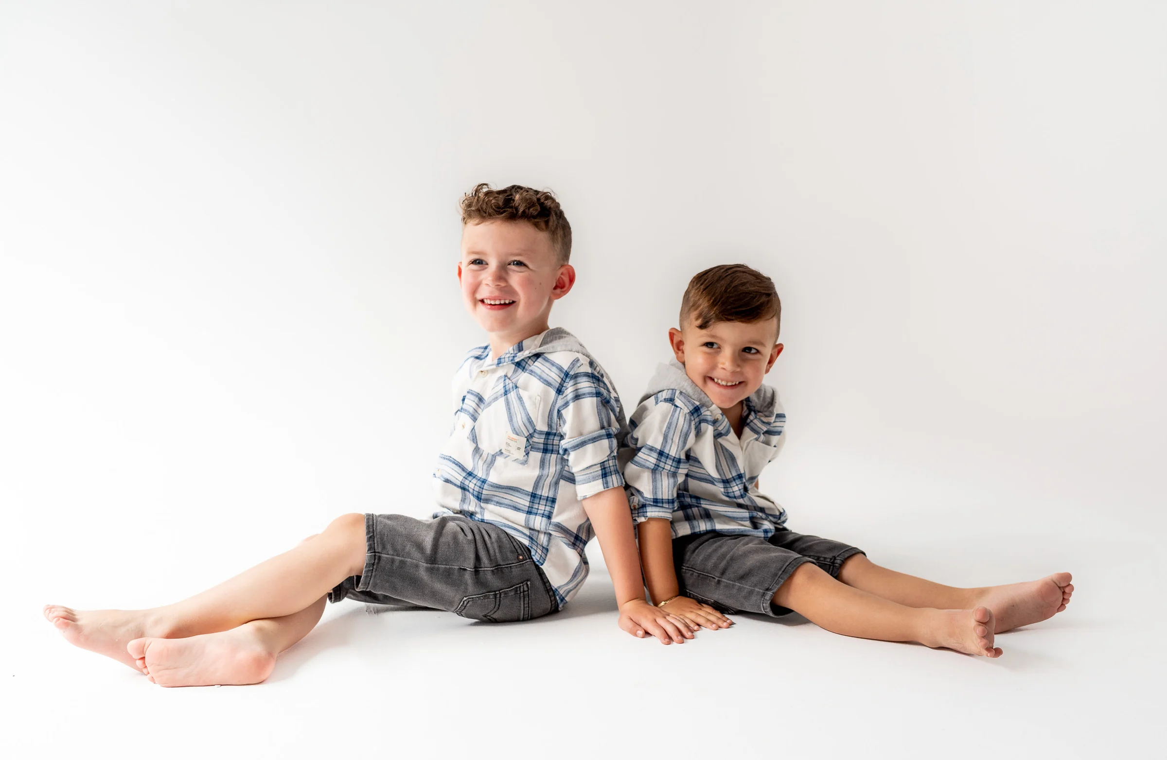 Dos niños sentados sobre fondo blanco en un retrato infantil de estudio.