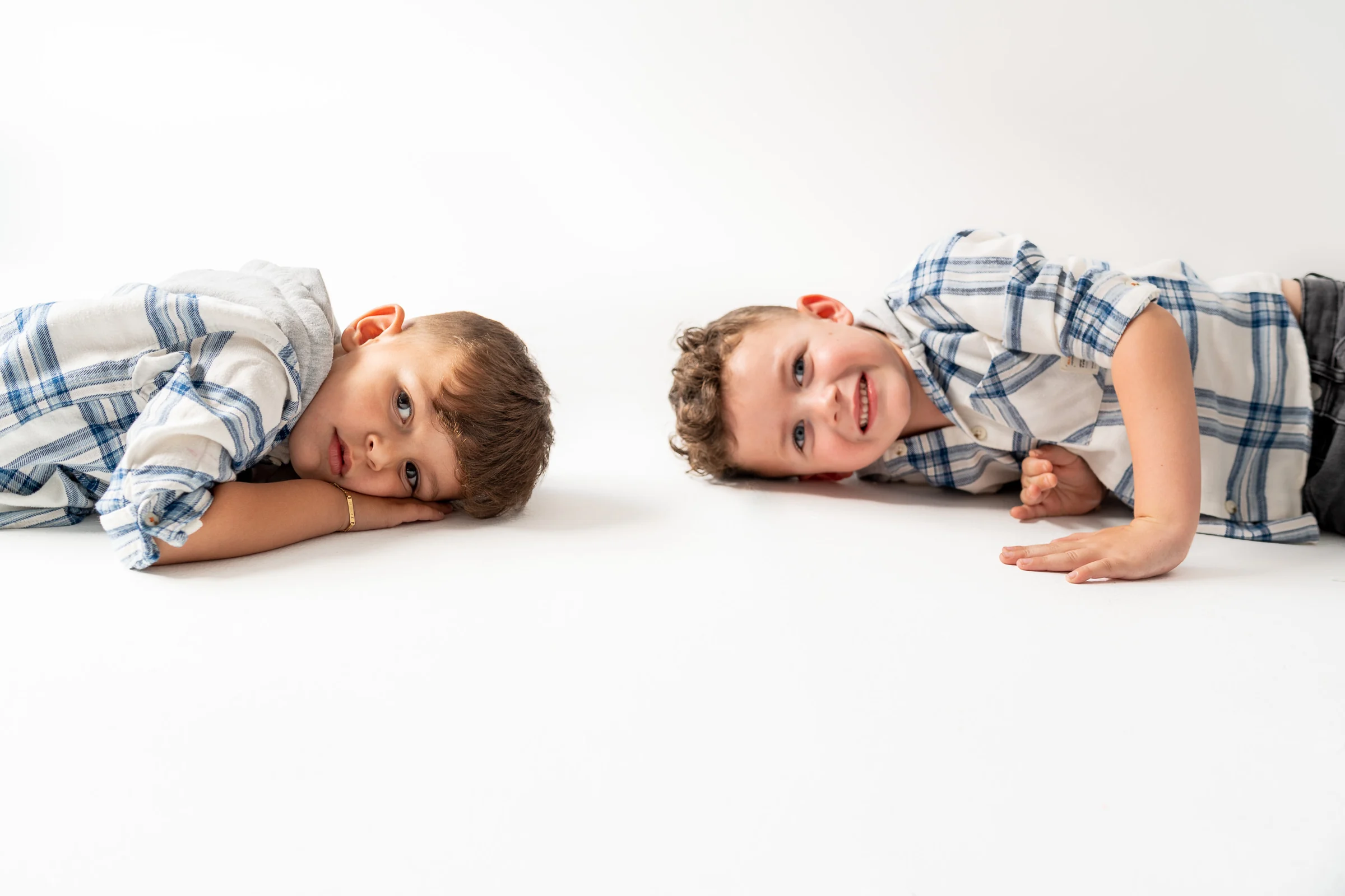 Dos niños tumbados sobre fondo blanco mirando a cámara en estudio.