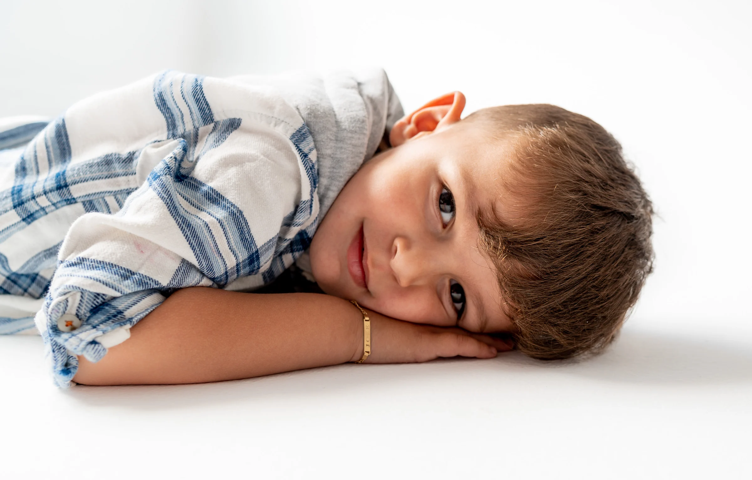 Retrato de niño tumbado sobre fondo blanco con camisa de cuadros azules.