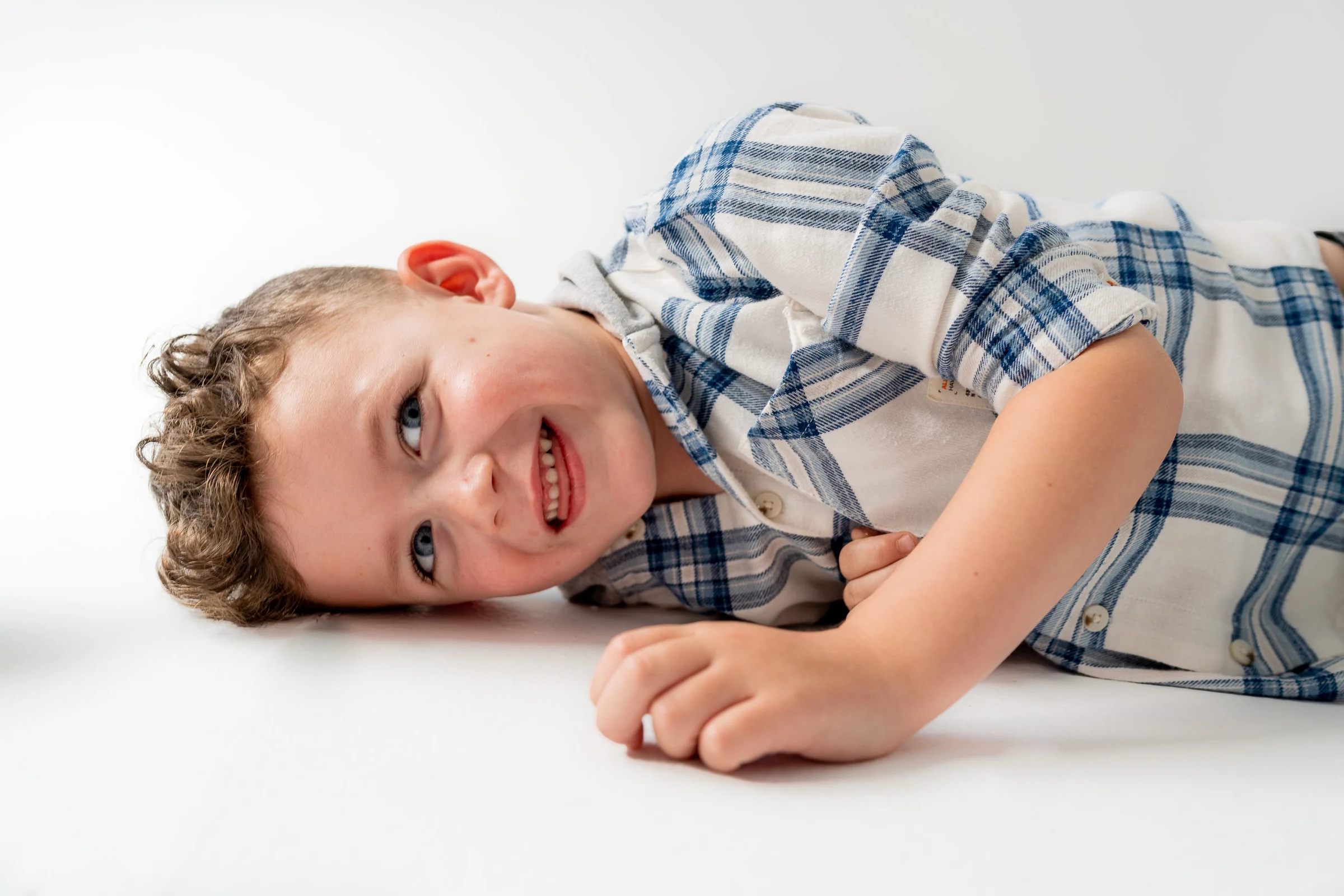 Primer plano de un niño sonriendo tumbado sobre fondo blanco de estudio.
