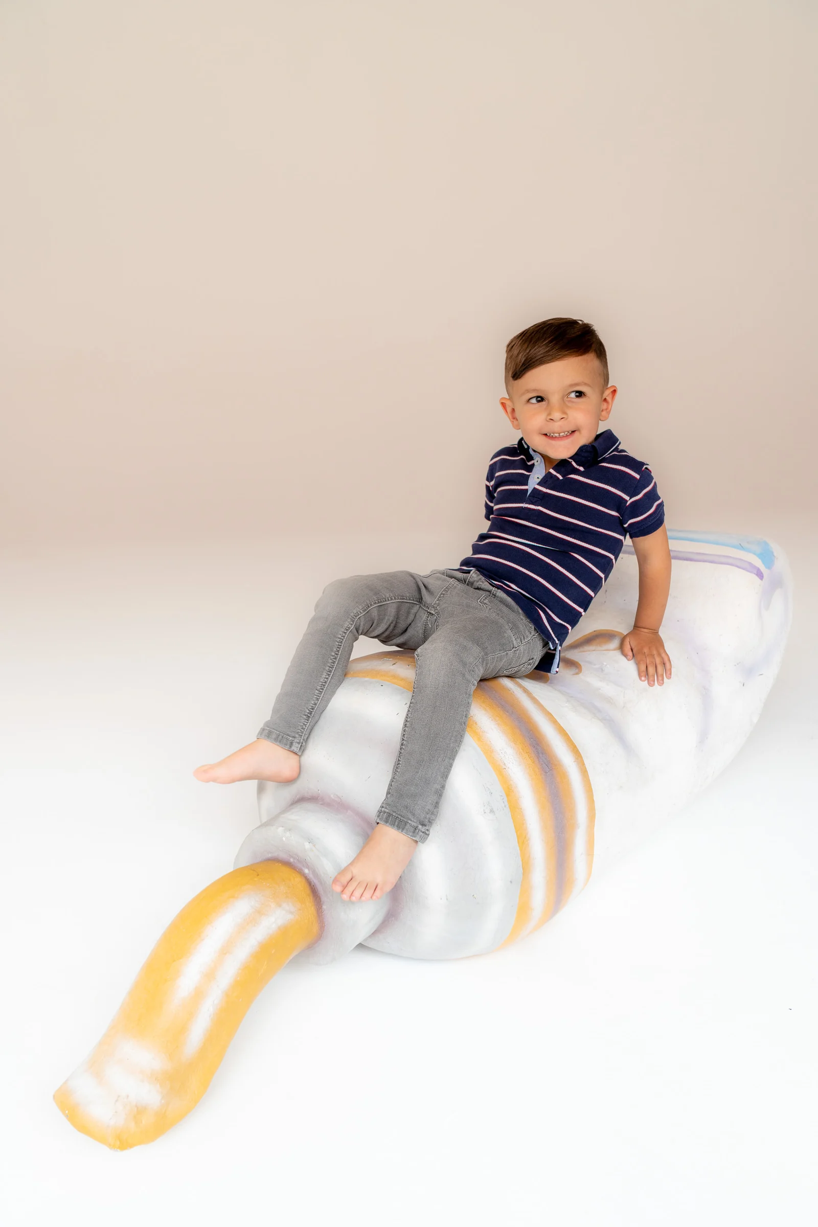 Niño posando sobre un atrezo con forma de caracola en fondo blanco de estudio.