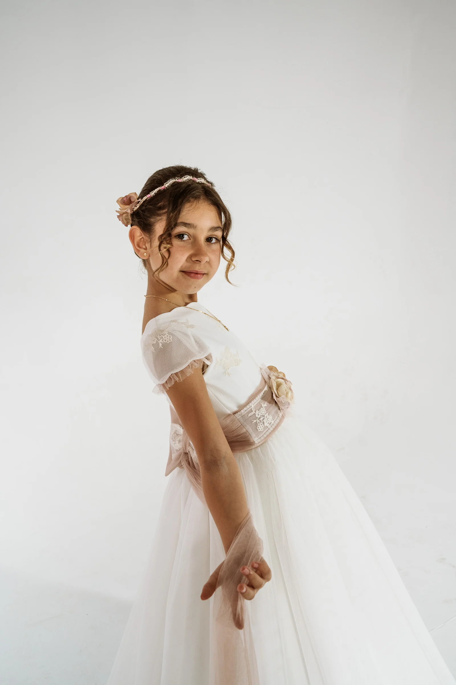 Niña con vestido de Primera Comunión posa de perfil sobre un fondo blanco en una sesión de estudio.