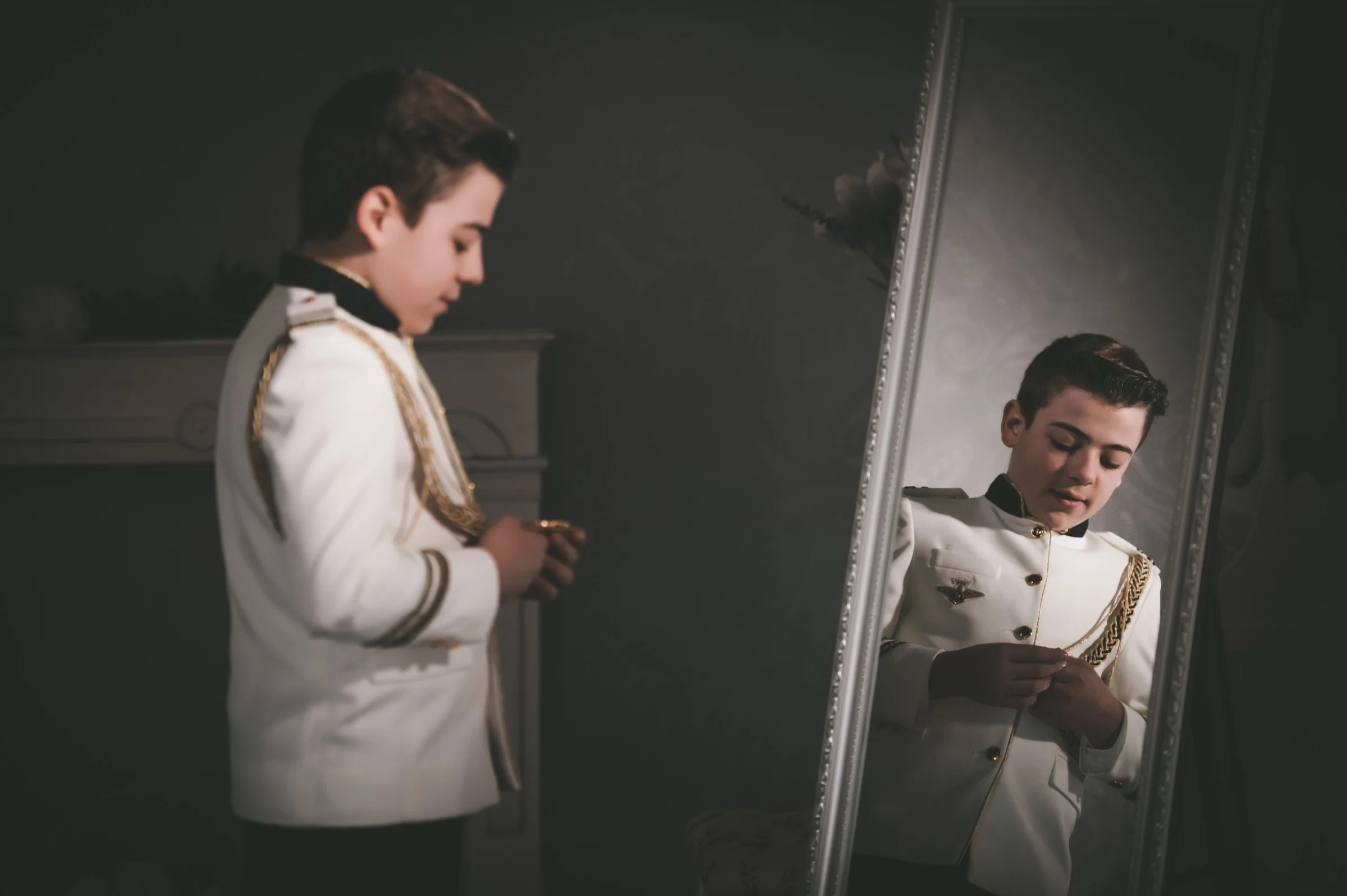 Niño termina de prepararse frente a un espejo con su traje de Primera Comunión en una escena de estudio.