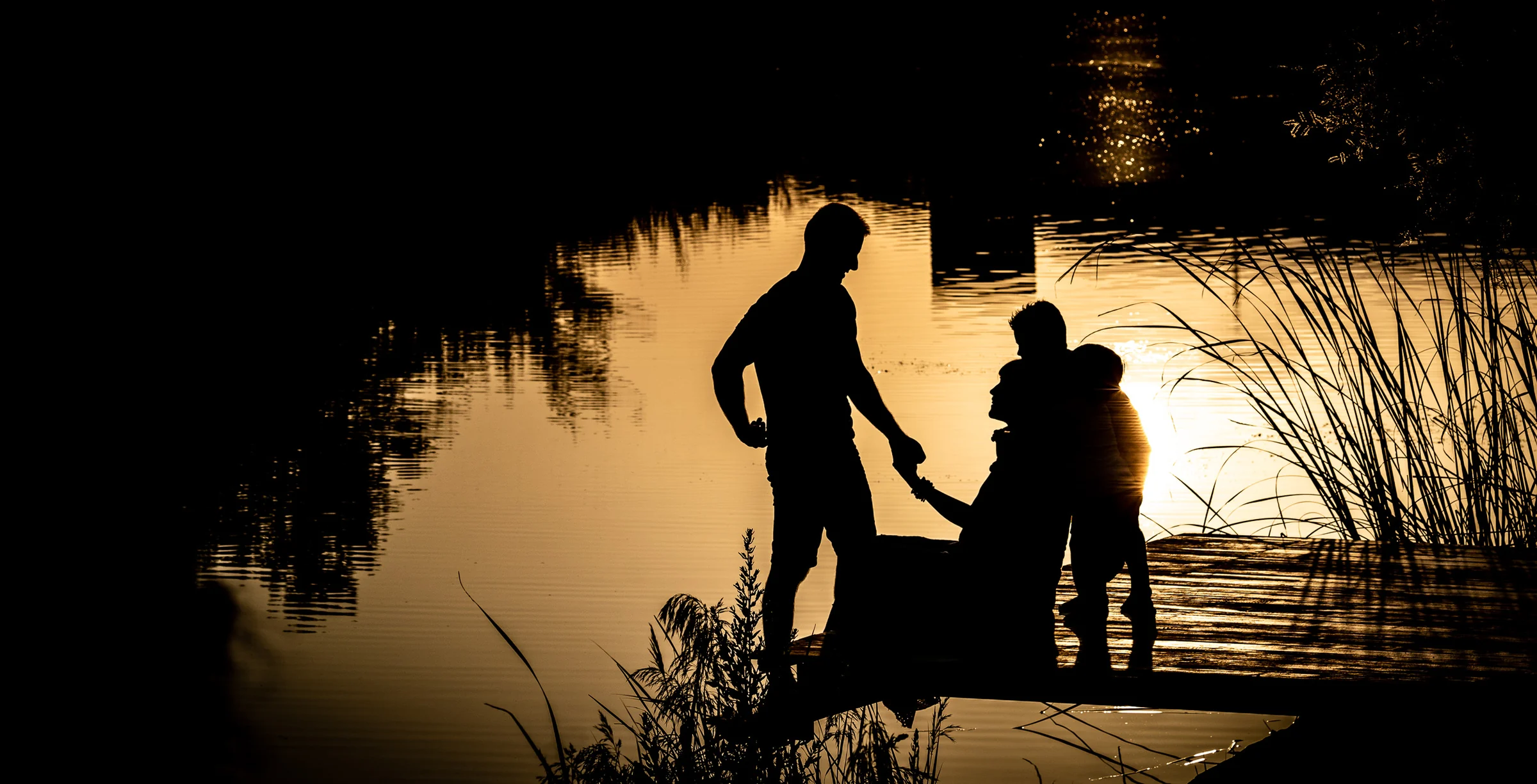 Siluetas de una familia junto a una mujer embarazada en un muelle durante el atardecer.