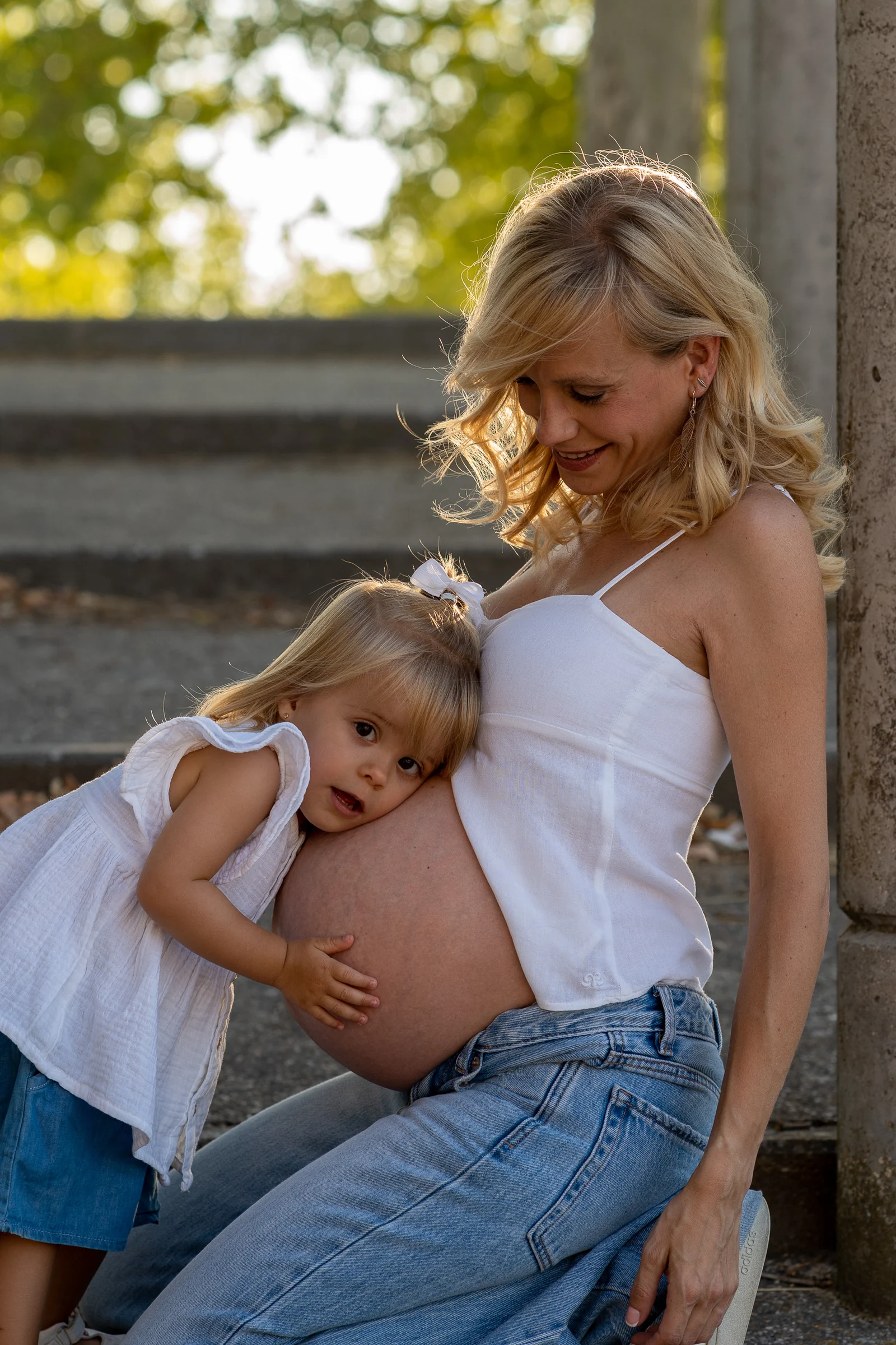 Niña apoya la cabeza sobre la barriga de su madre embarazada mientras ambas comparten un momento cariñoso.