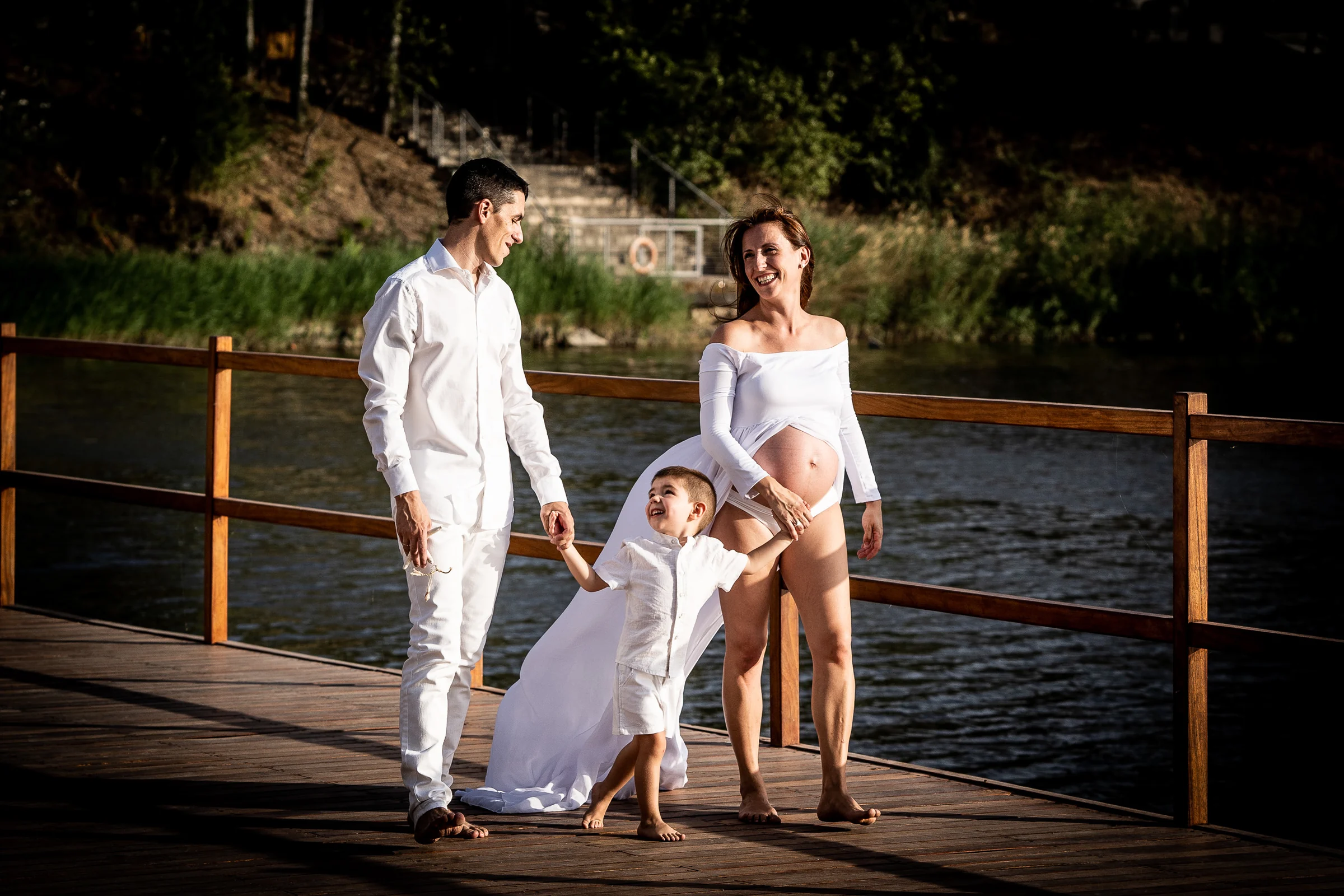 Padre, madre embarazada y su hijo caminan juntos por un muelle de madera junto al lago.