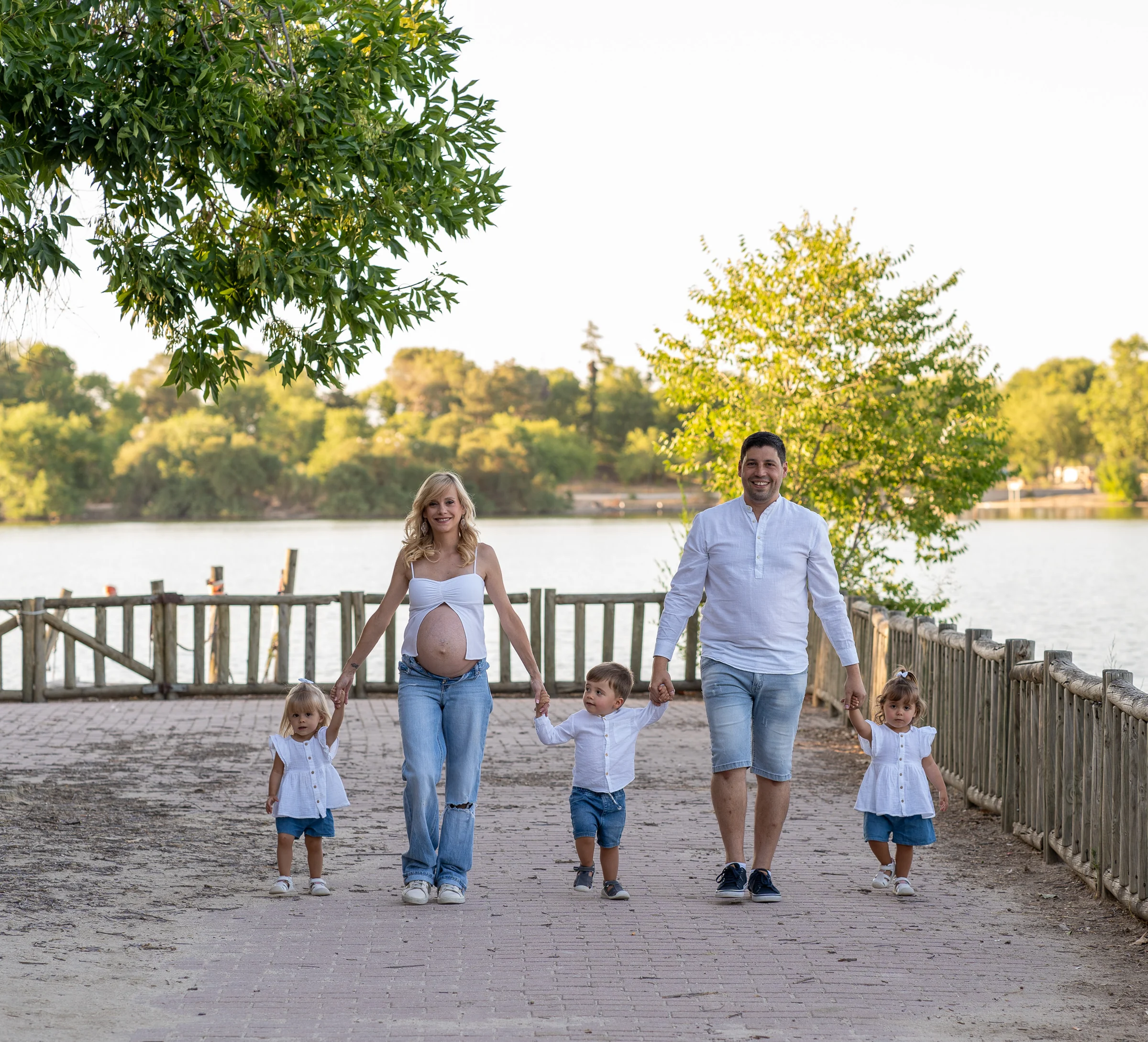 Familia con una mujer embarazada, su pareja y tres niños camina de la mano por un paseo junto al lago.