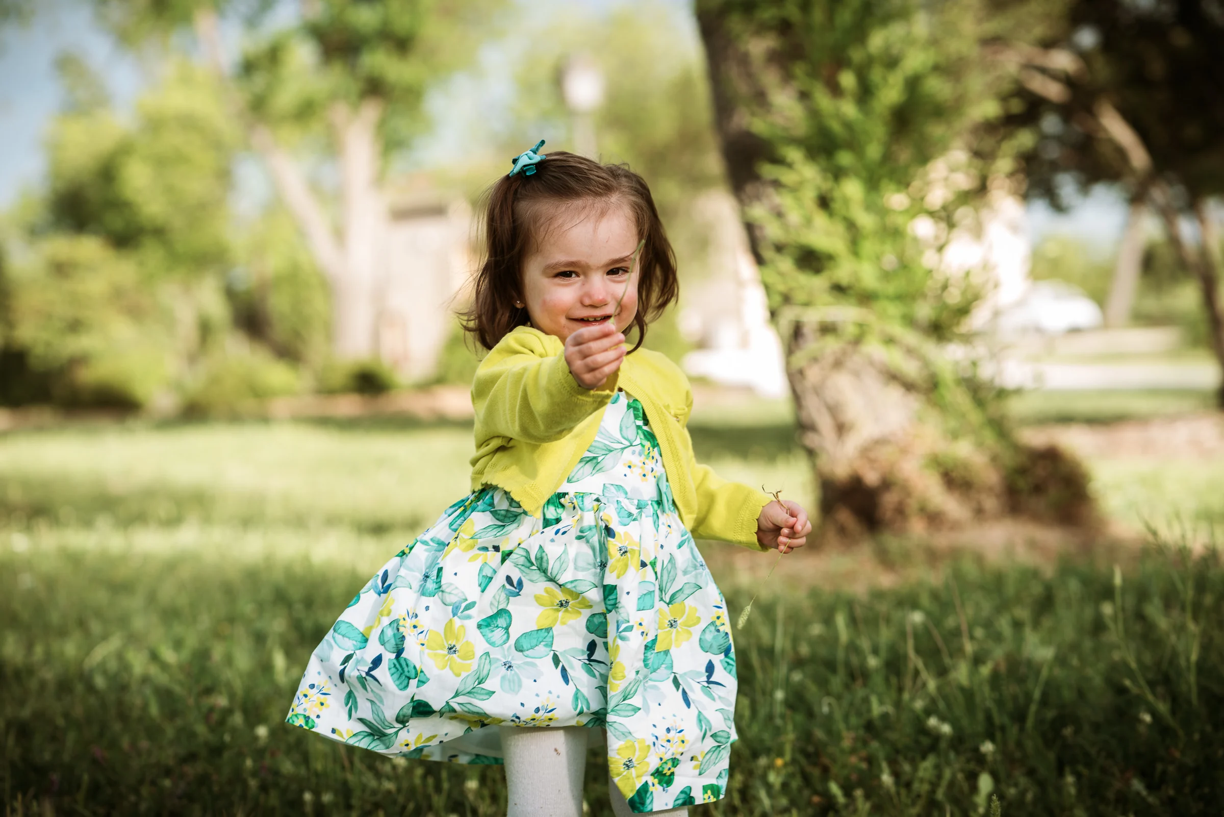 Niña pequeña con vestido floral juega y se mueve sobre el césped en un parque.