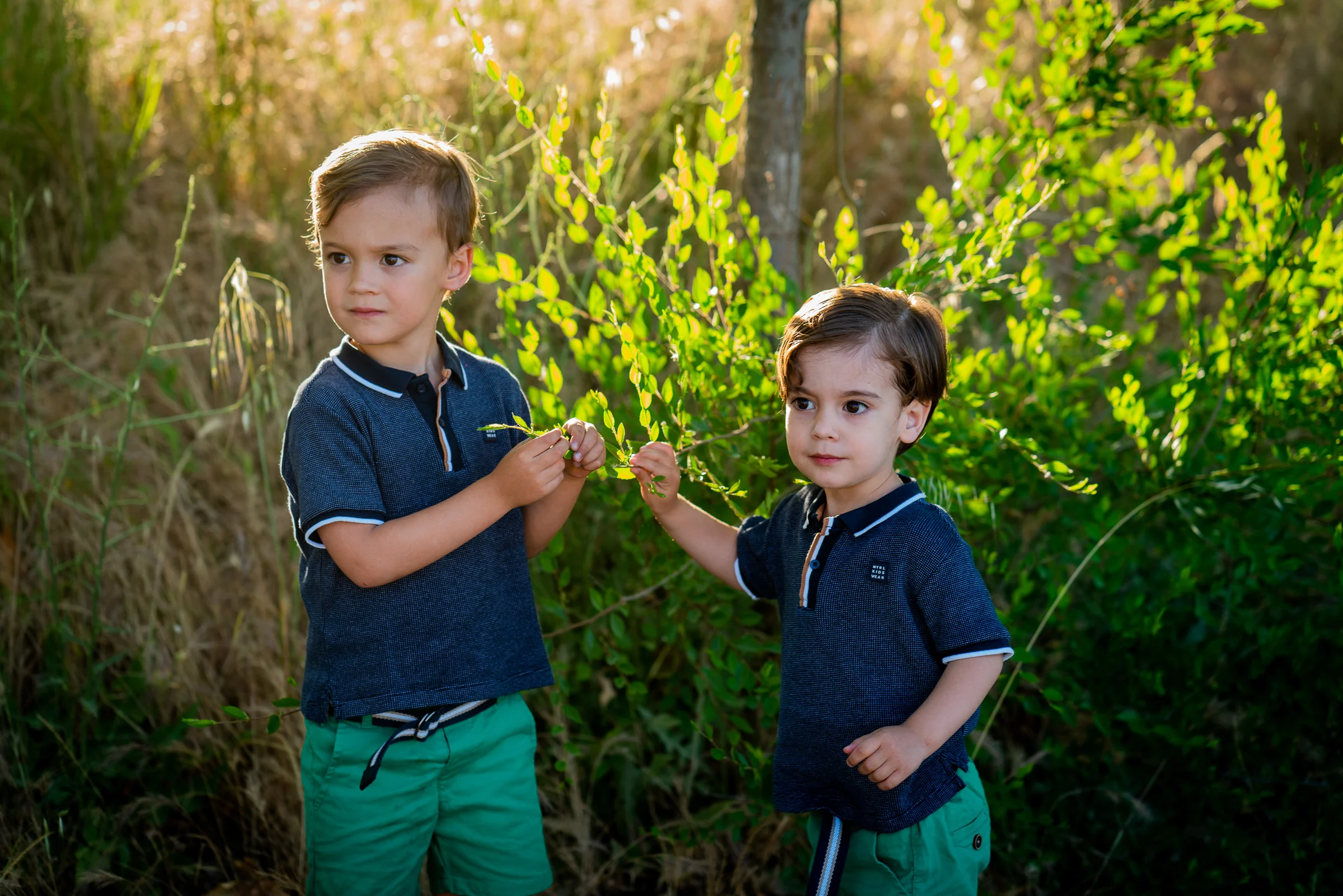 Dos hermanos pequeños con polos azules posan juntos entre la vegetación.