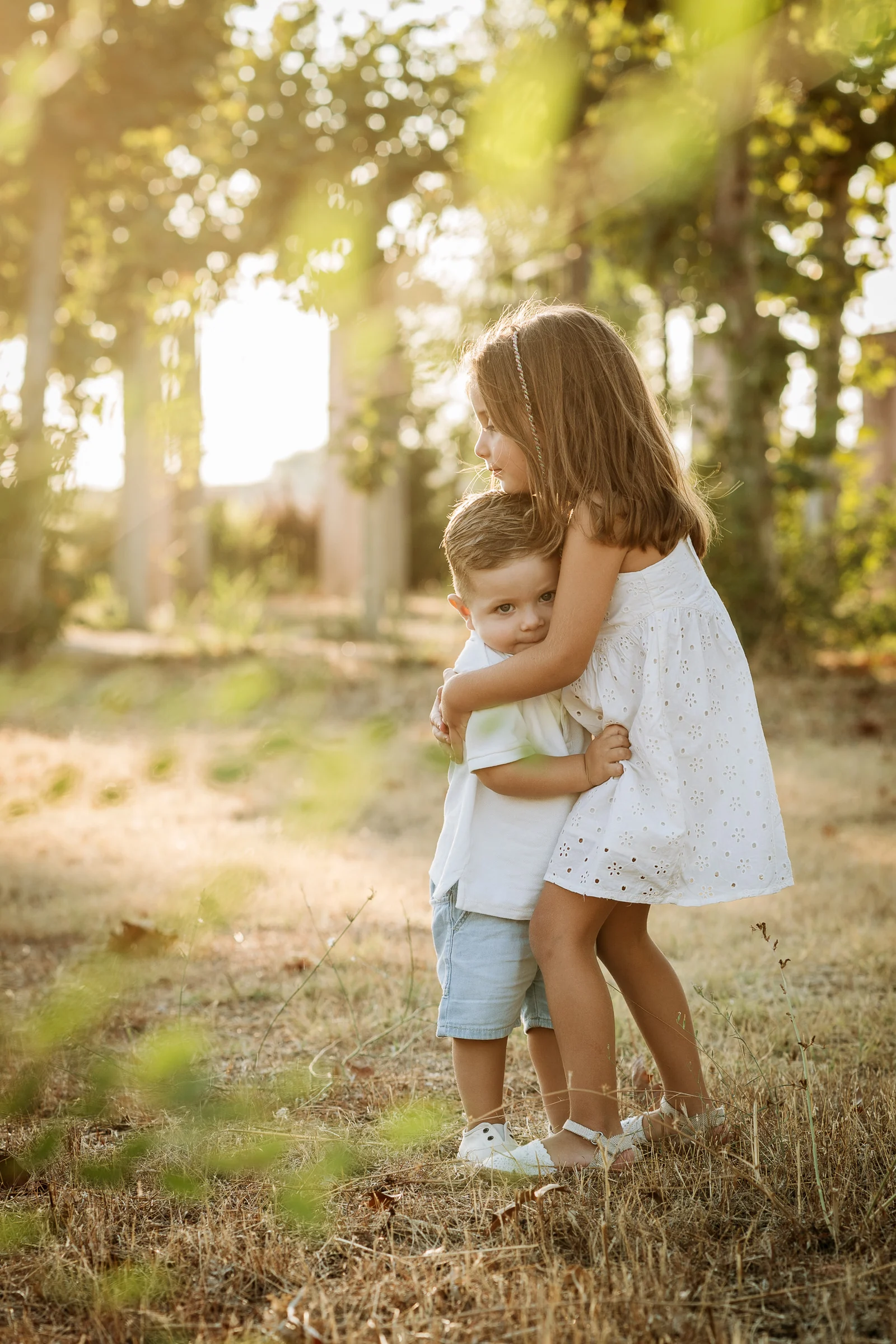 Hermana mayor abraza a su hermano pequeño durante una sesión familiar con luz de atardecer.