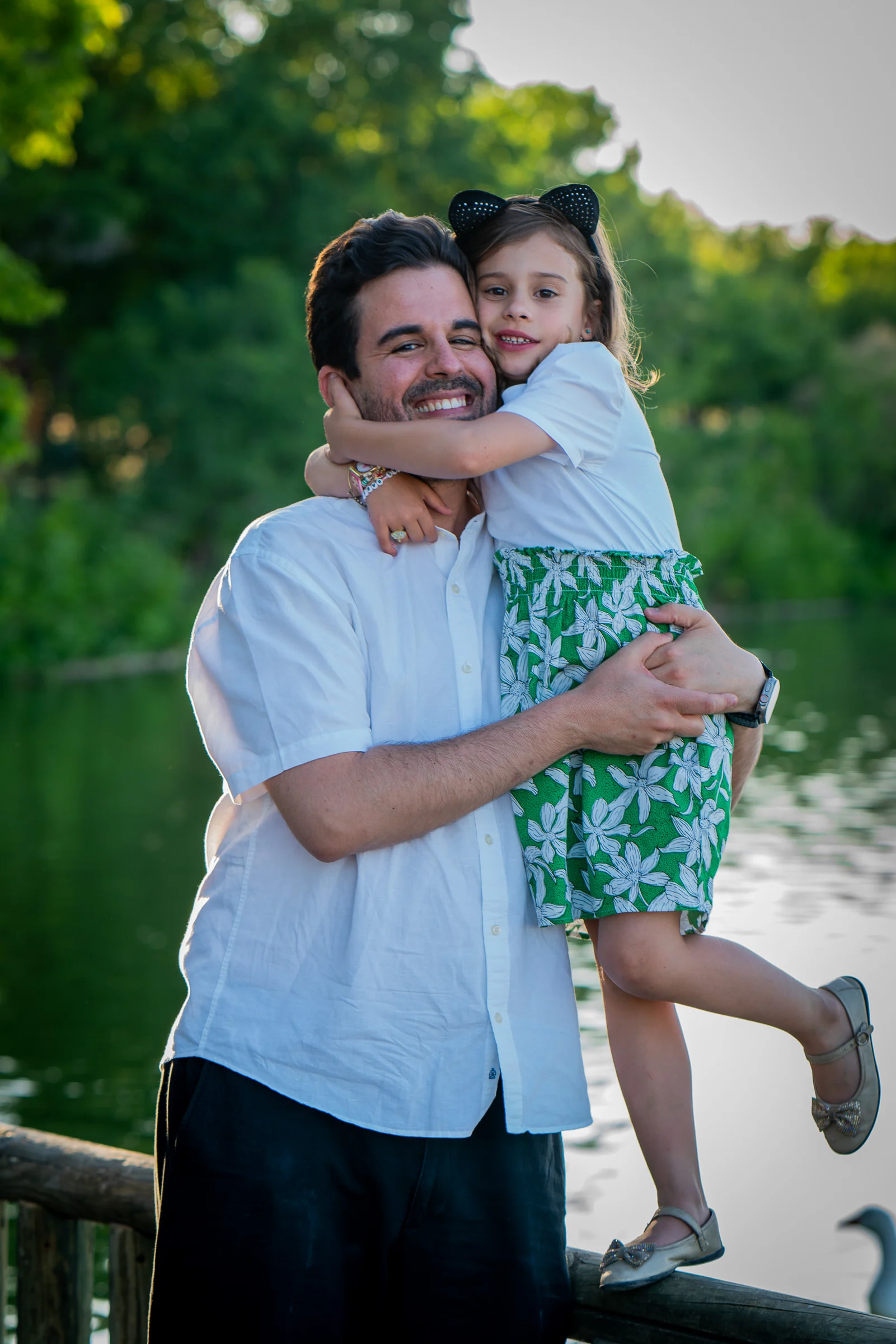 Padre sonríe mientras sostiene en brazos a su hija junto a un lago.