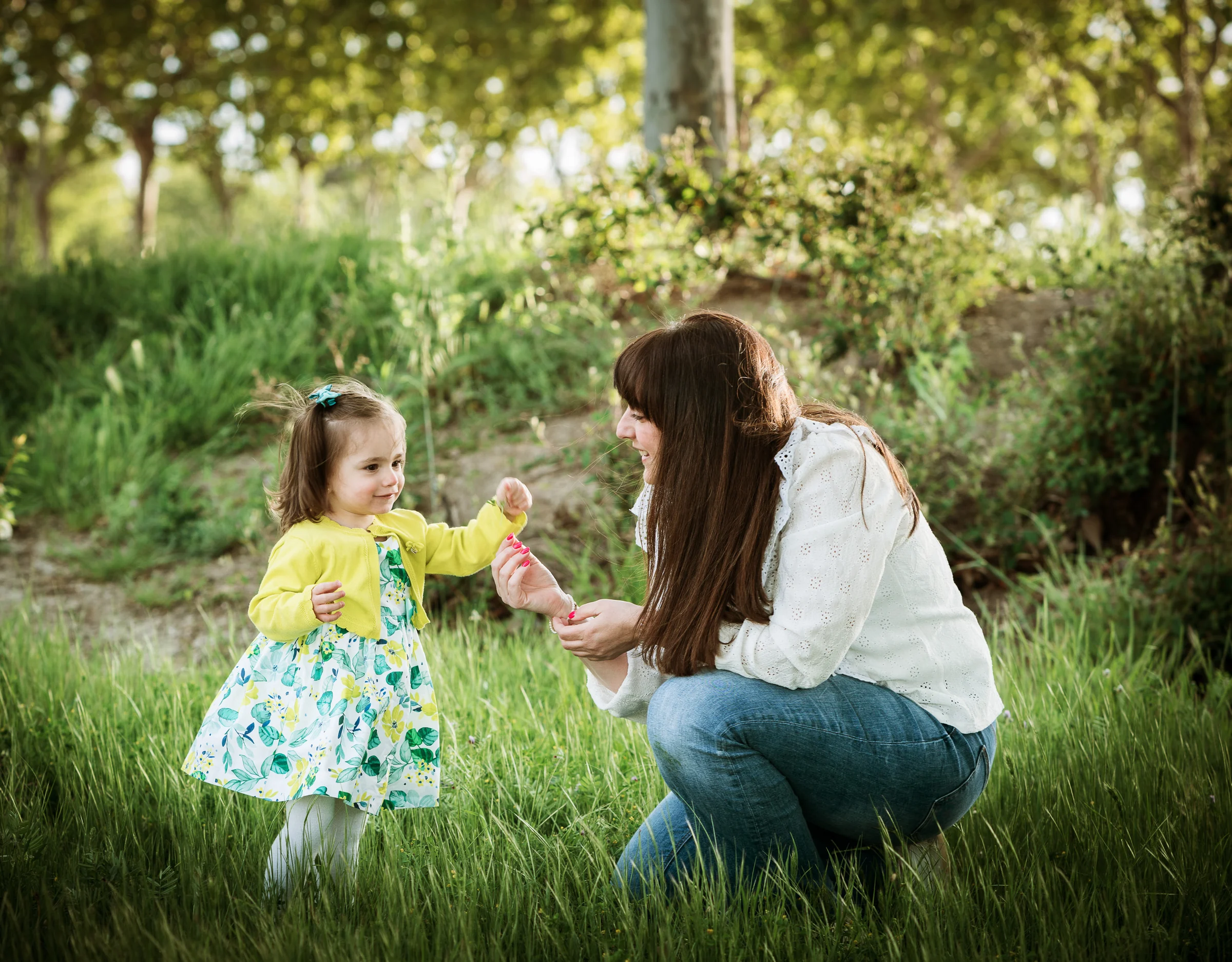 Madre e hija juegan juntas sobre la hierba durante una sesión familiar al aire libre.