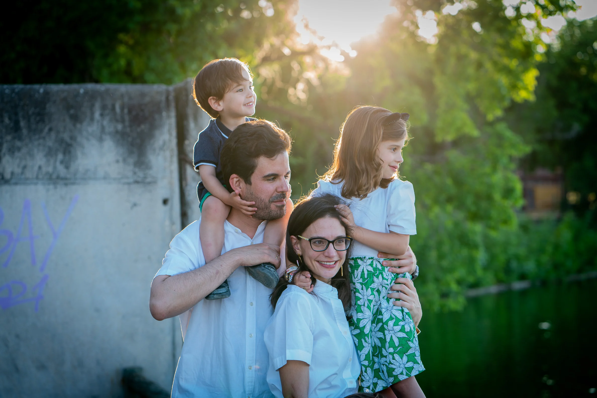 Familia de cinco se reúne junto a un lago con los niños subidos a los hombros de sus padres.