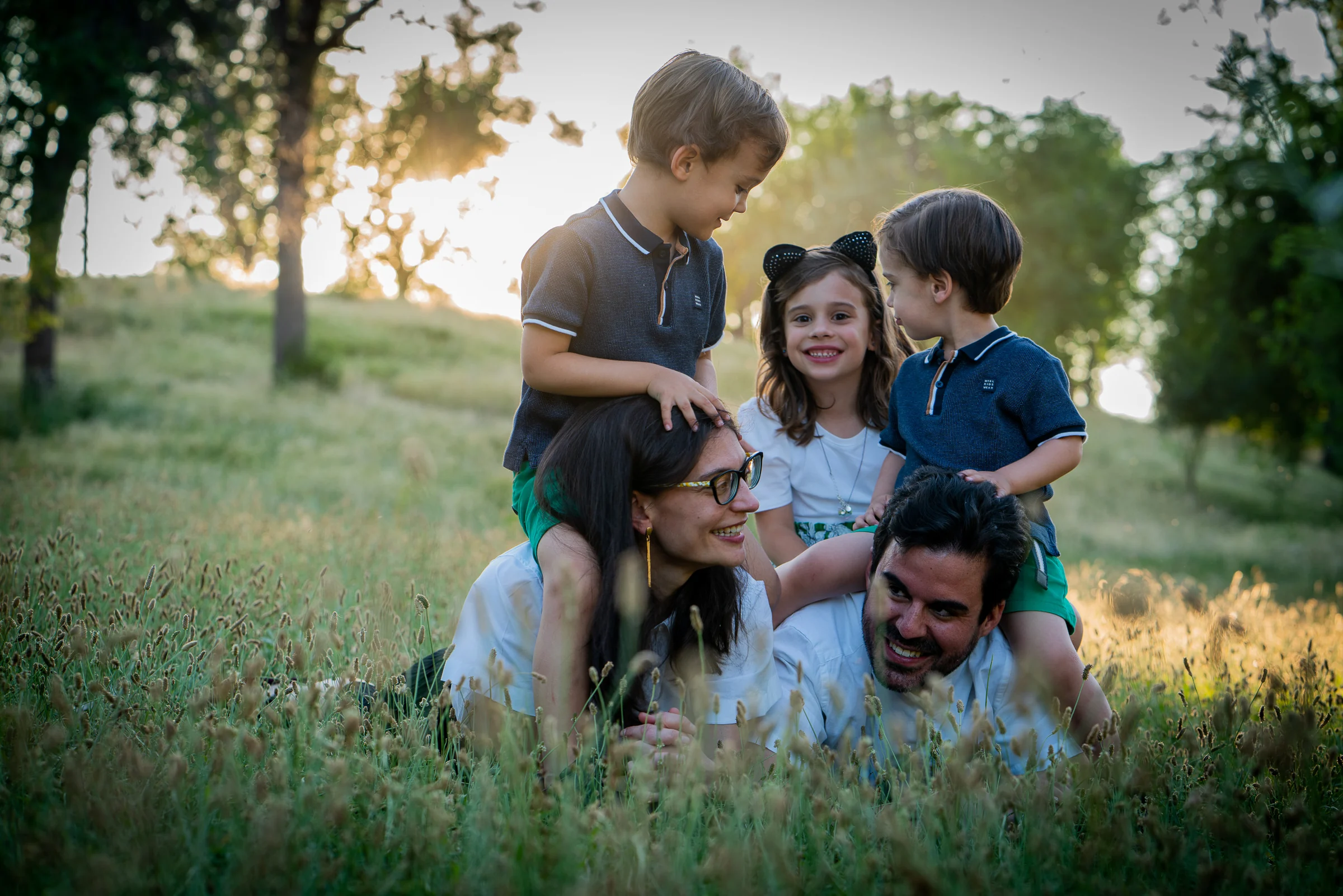 Familia de cinco se reúne sentada sobre la hierba durante una sesión al atardecer.