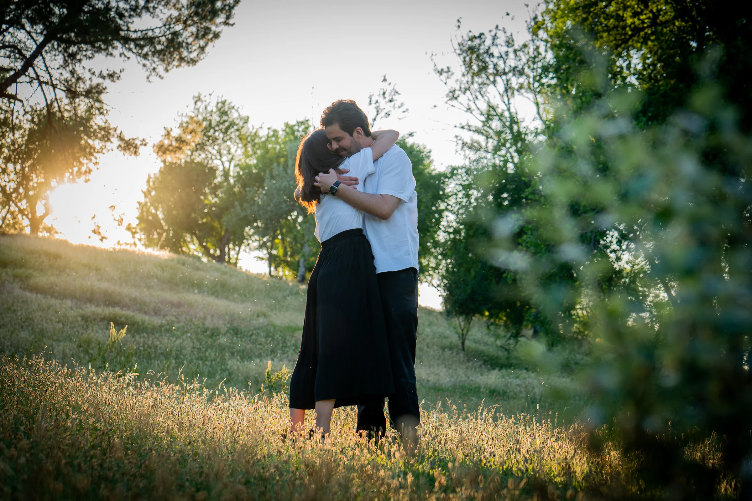 Pareja se abraza en un parque durante una sesión familiar al atardecer.