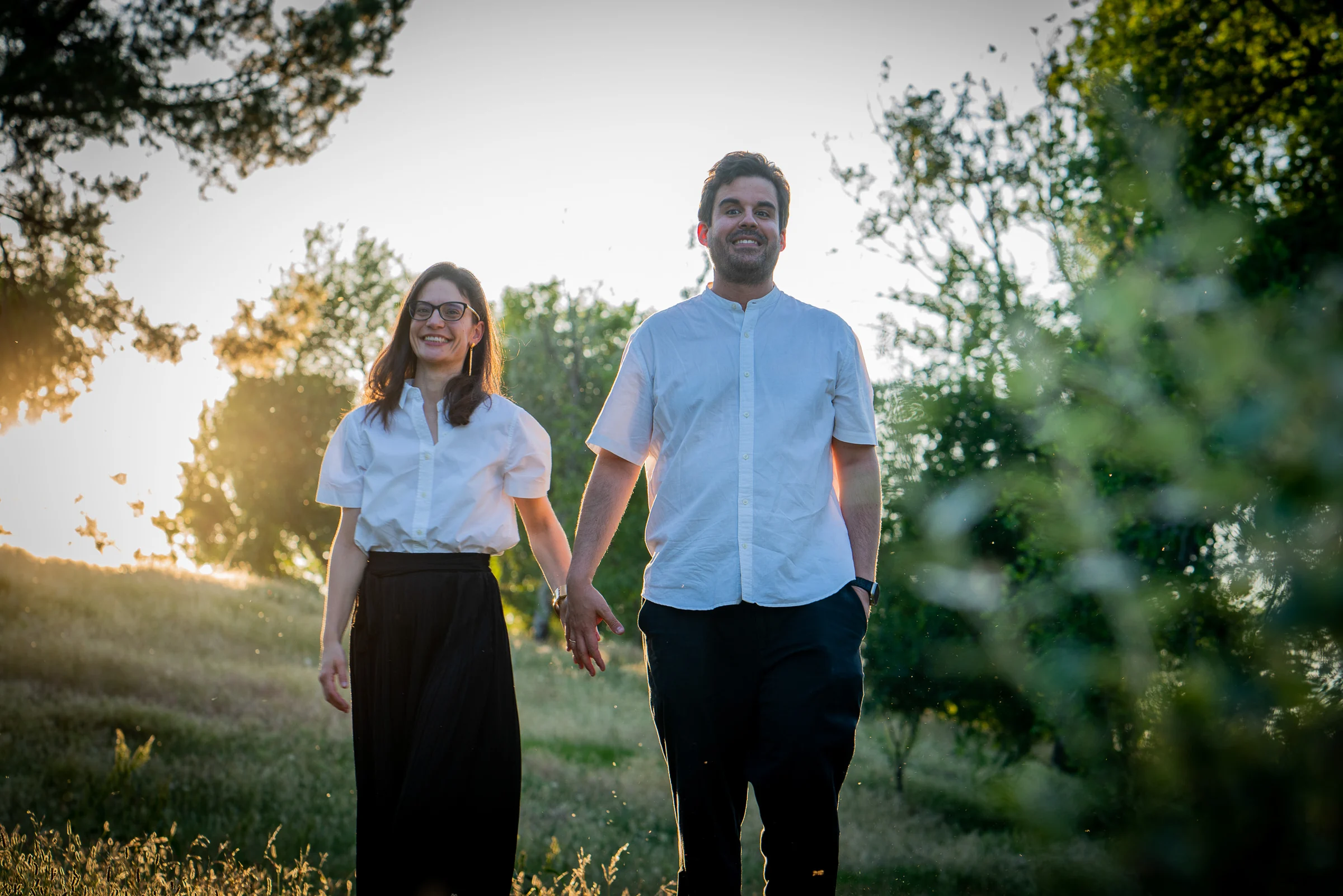 Pareja camina de la mano por un parque iluminado por la luz del atardecer.