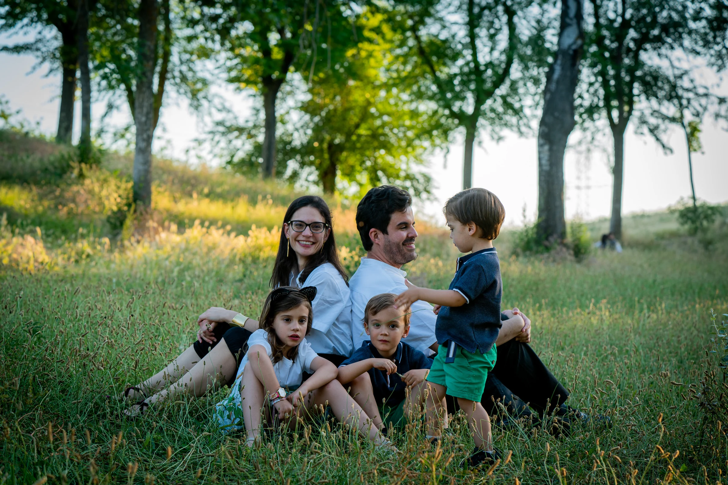 Familia de cinco posa sentada entre la hierba en un parque al atardecer.